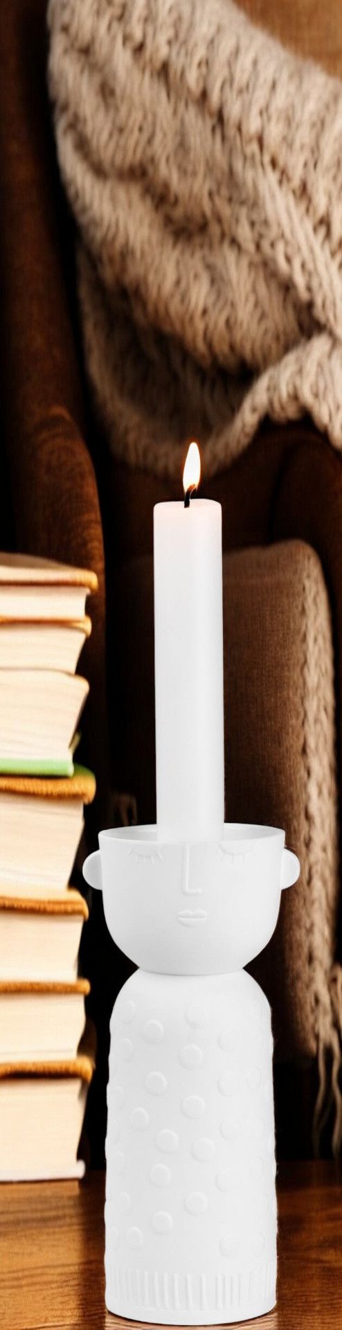 Weißer Porzellan Kerzenhalter "Luna" von Räder mit brennender Kerze, Bücherstapel und Sessel im Hintergrund.