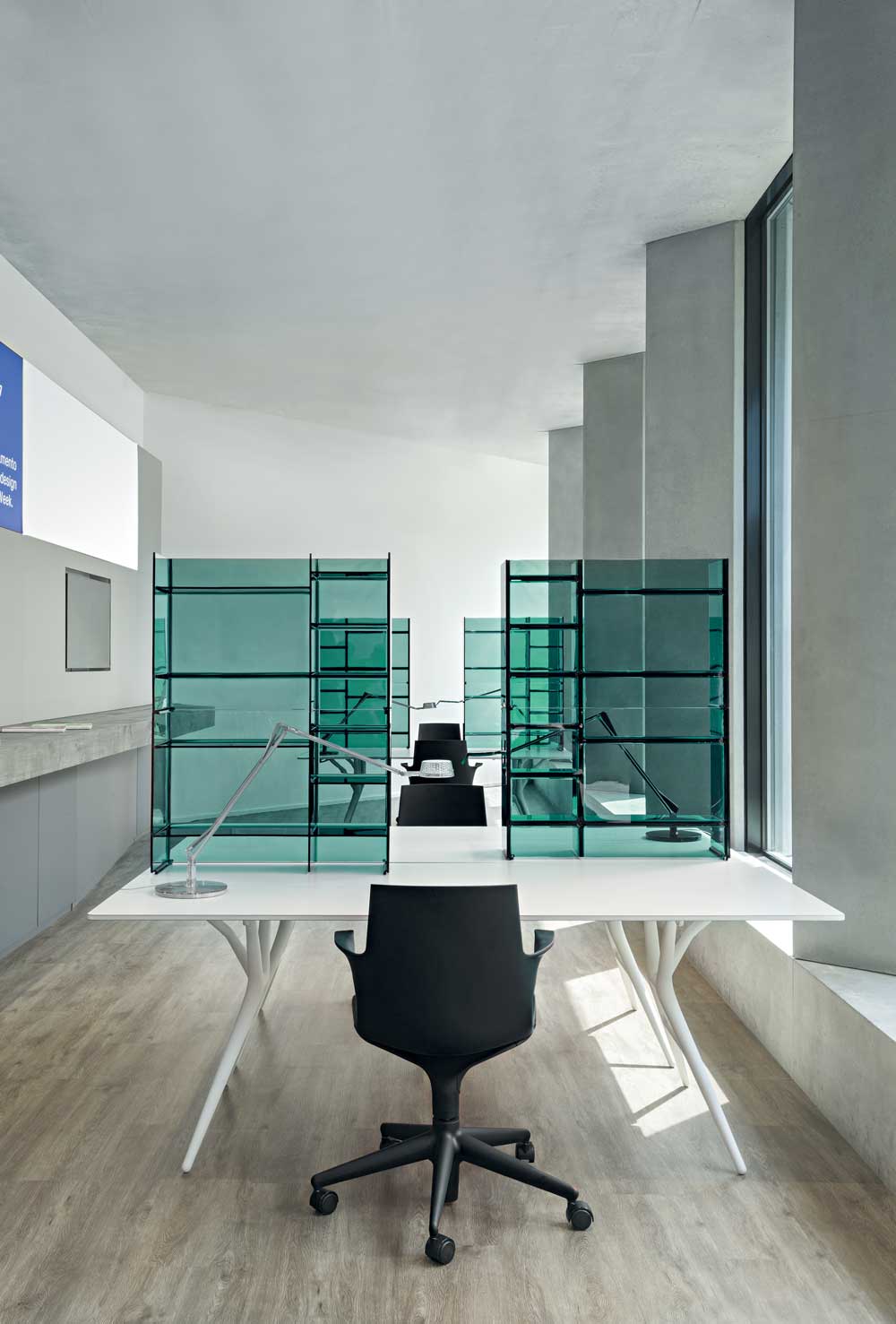 Heller Büroraum mit Spoon Table (Kartell) und transparenten, grünen Raumteilern. Moderner Schreibtisch mit Bürostuhl.