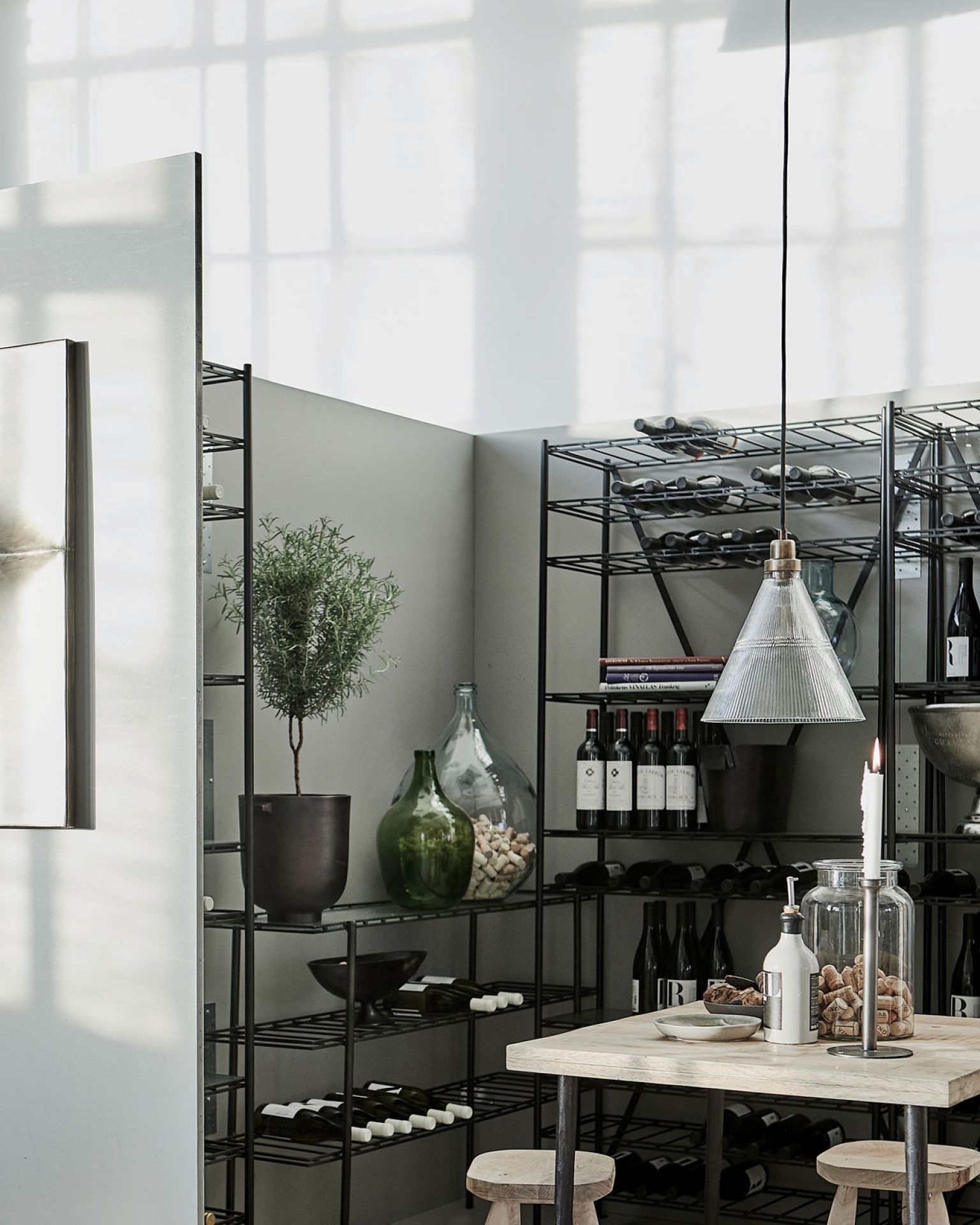 Vira Pendelleuchte von House Doctor über Esstisch mit Weinflaschen im Hintergrund, moderne Innenraumbeleuchtung.