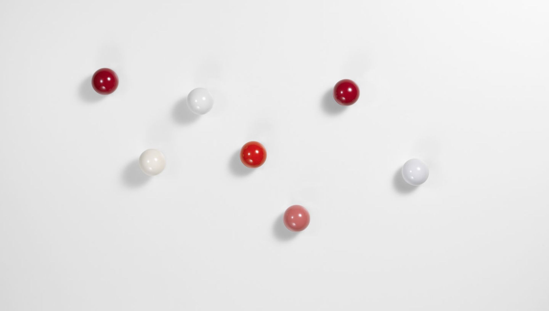 Vitra Coat Dots Garderobenhaken 3er-Set in Rot- und Weißtönen an einer weißen Wand.