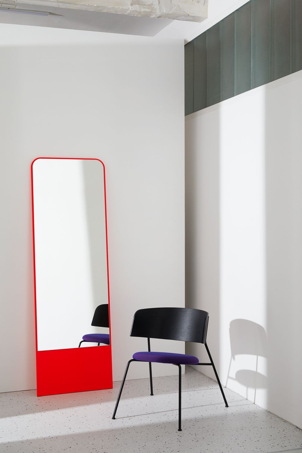 FRIEDRICH Spiegel mit rotem Rahmen neben einem Stuhl in minimalistischem Raum.