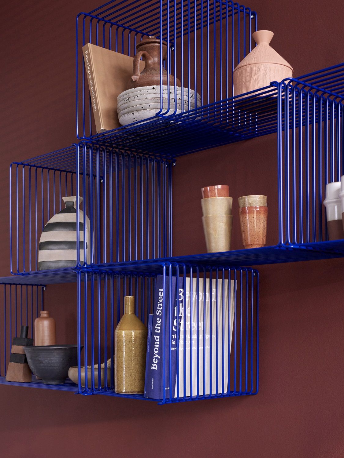 Blaues Montana Wire Cube Drahtregal an einer Wand, dekoriert mit Büchern und Keramik.