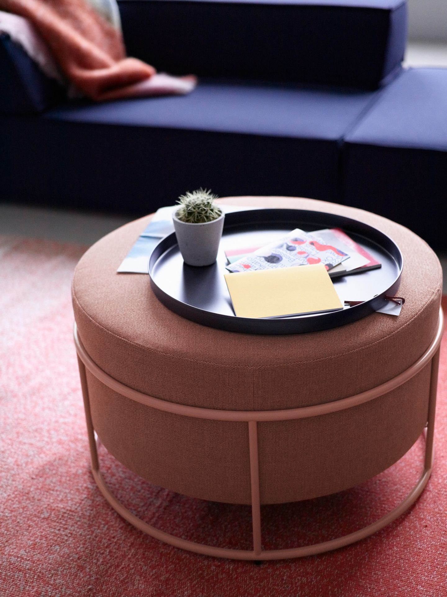 Nahaufnahme des Cor Drop Hockers (Ø 79 cm) in Koralle mit Ablage und Dekoration.