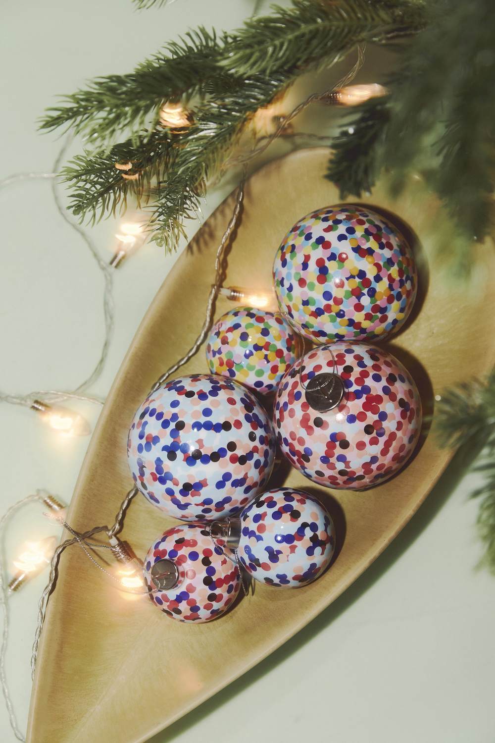 Mehrere Alessi Proust Weihnachtskugeln AM43 mit bunten Punkten in einer Holzschale mit Lichterkette.