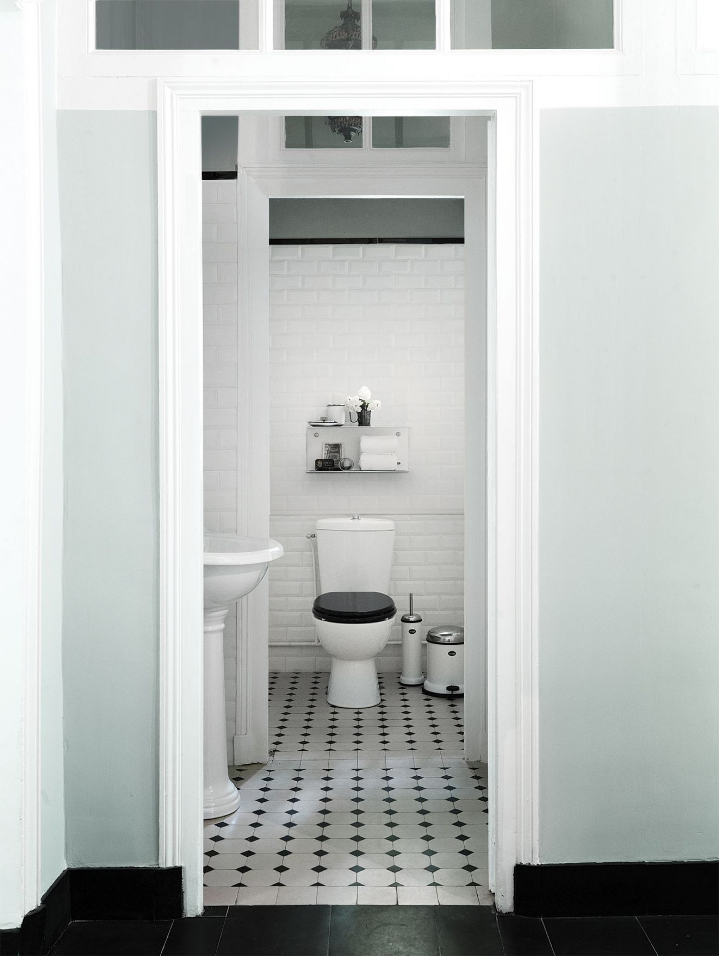 Helles Badezimmer mit weißer Toilette, Vipp WC-Bürste und Mülleimer auf einem schwarz-weiß gemusterten Boden.