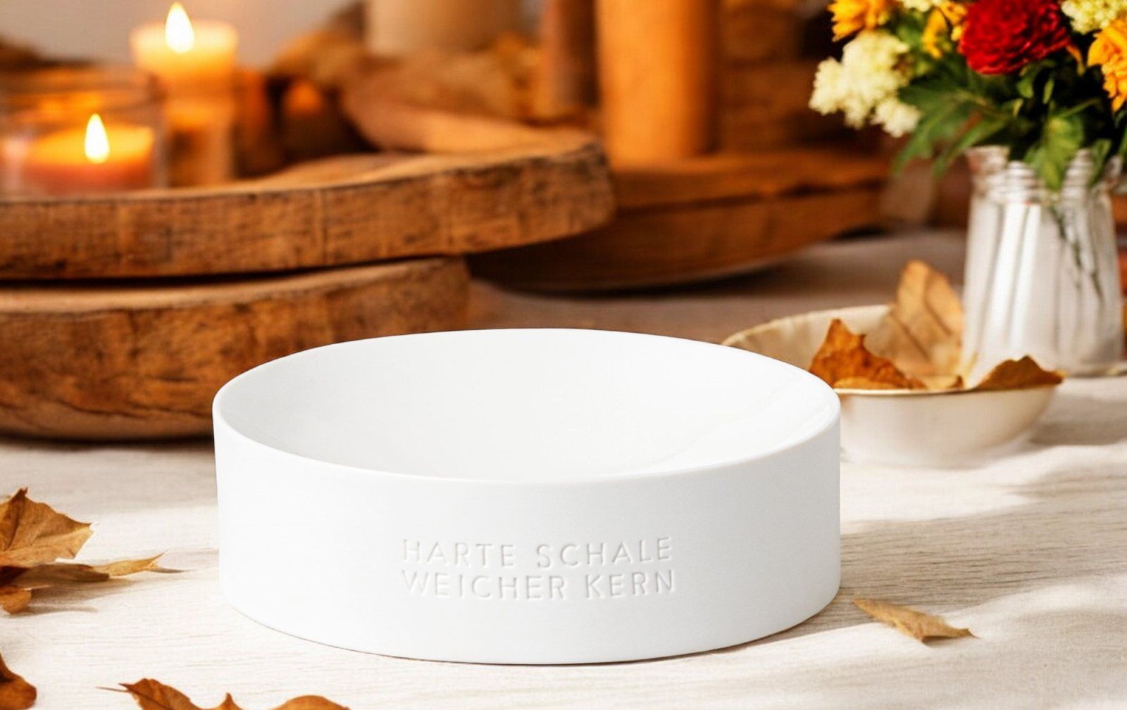 Weiße "Harte Schale weicher Kern" Schale als Deko-Element auf Tisch mit Herbstdekoration.