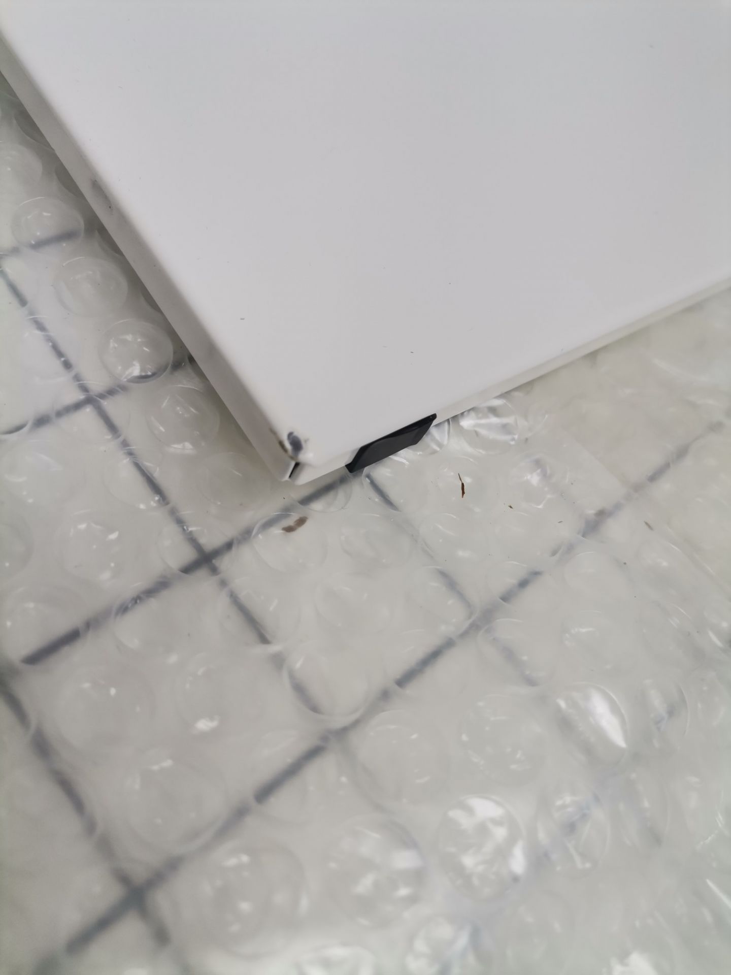 Detailaufnahme eines weißen USM Haller Ersatzteils mit Beschädigung, verpackt in Luftpolsterfolie.