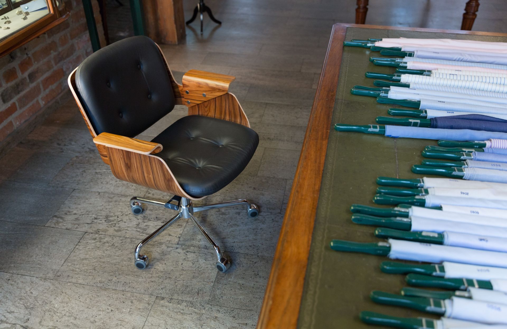 D49 Tecta Schreibtischstuhl: Schwarzer Leder Bürostuhl mit Holzarmlehnen und Chromfußkreuz auf Fliesenboden.