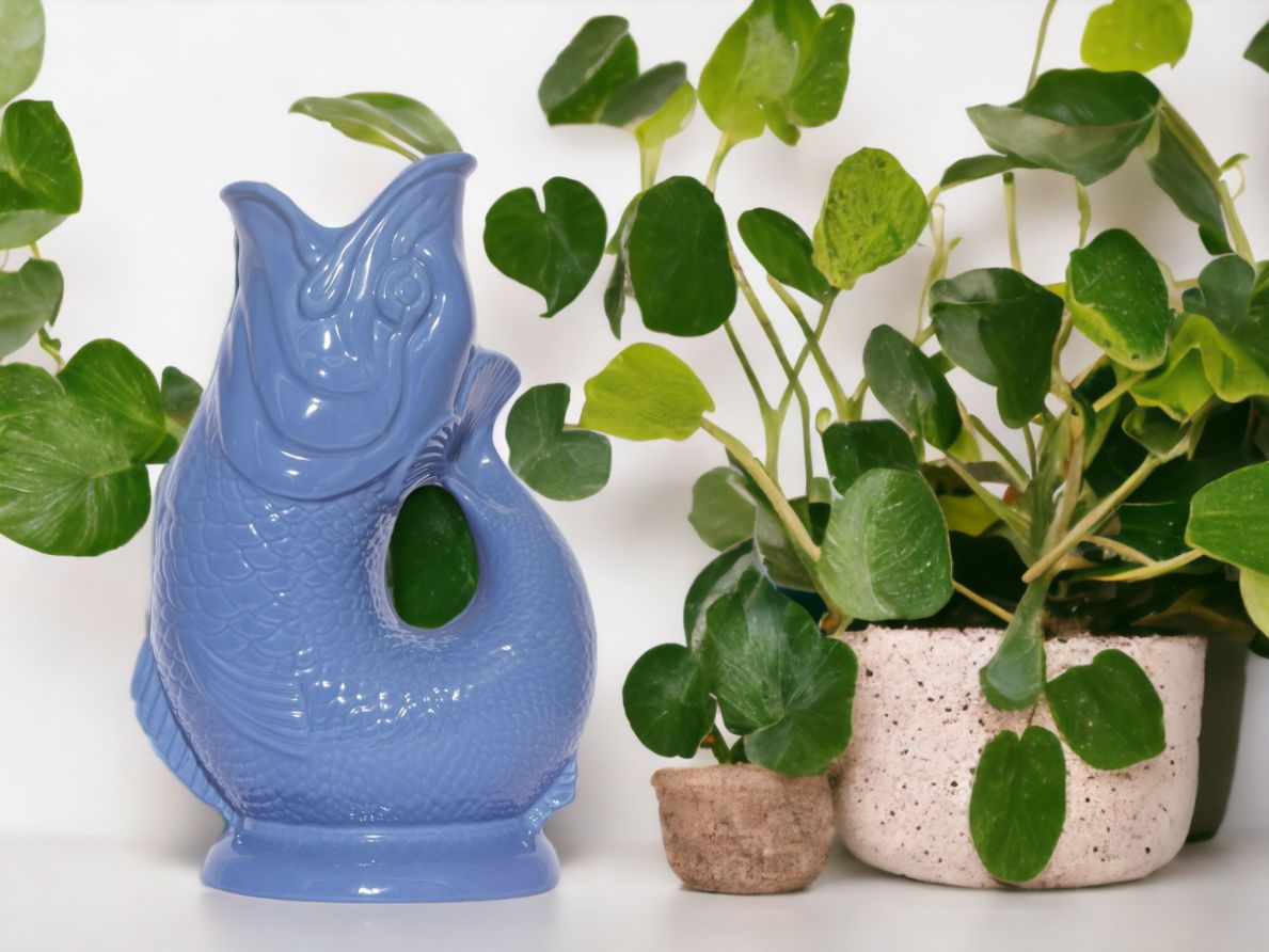 Blau-graue Gluckigluck Fischkaraffe neben grünen Zimmerpflanzen. Dekorative Vase im Fischdesign.