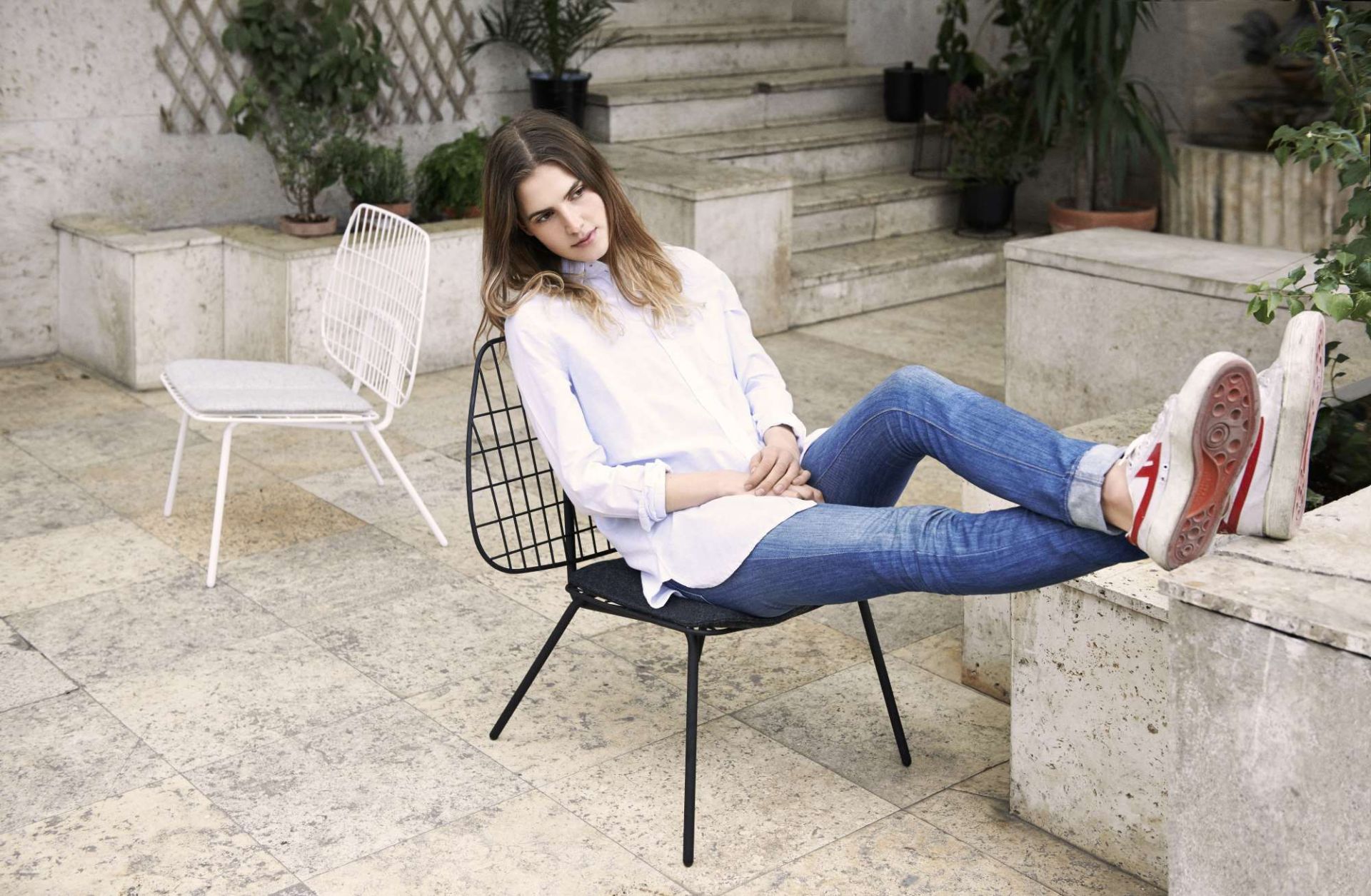 Frau entspannt auf einem schwarzen WM String Lounge Chair Sessel von Audo im Außenbereich.