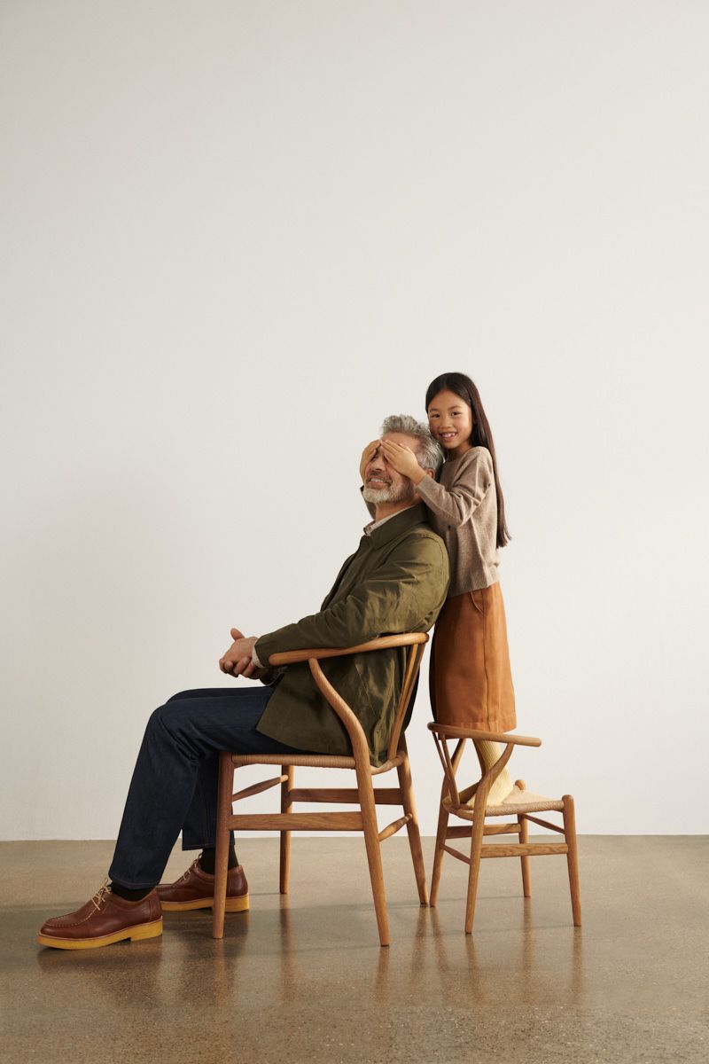 Mann sitzt auf CH24 Wishbone Stuhl, Mädchen steht dahinter auf Kinderstuhl.