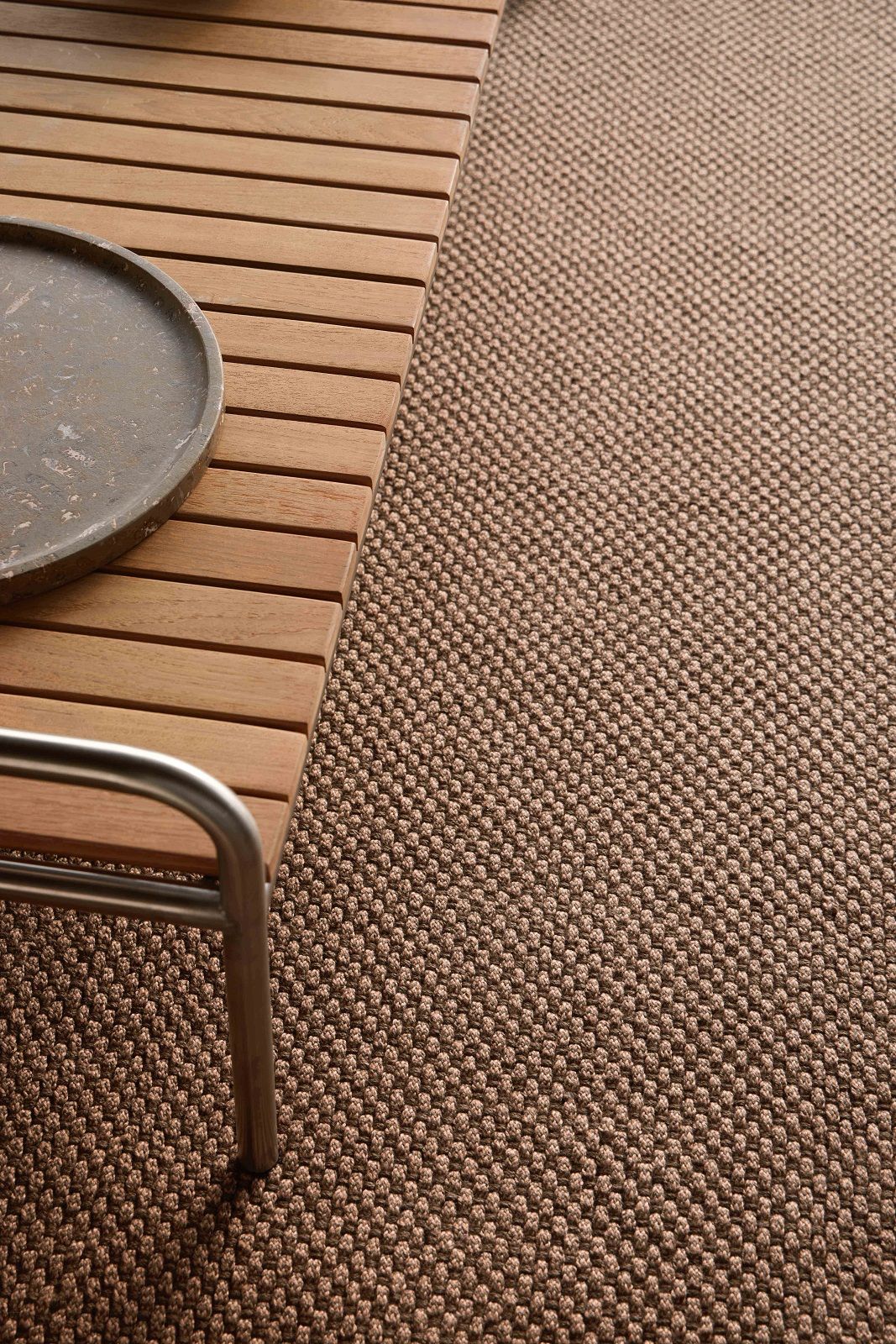 Detailaufnahme des braunen Saline Outdoor Teppichs von Gan neben einer Holzbank mit Tablett.