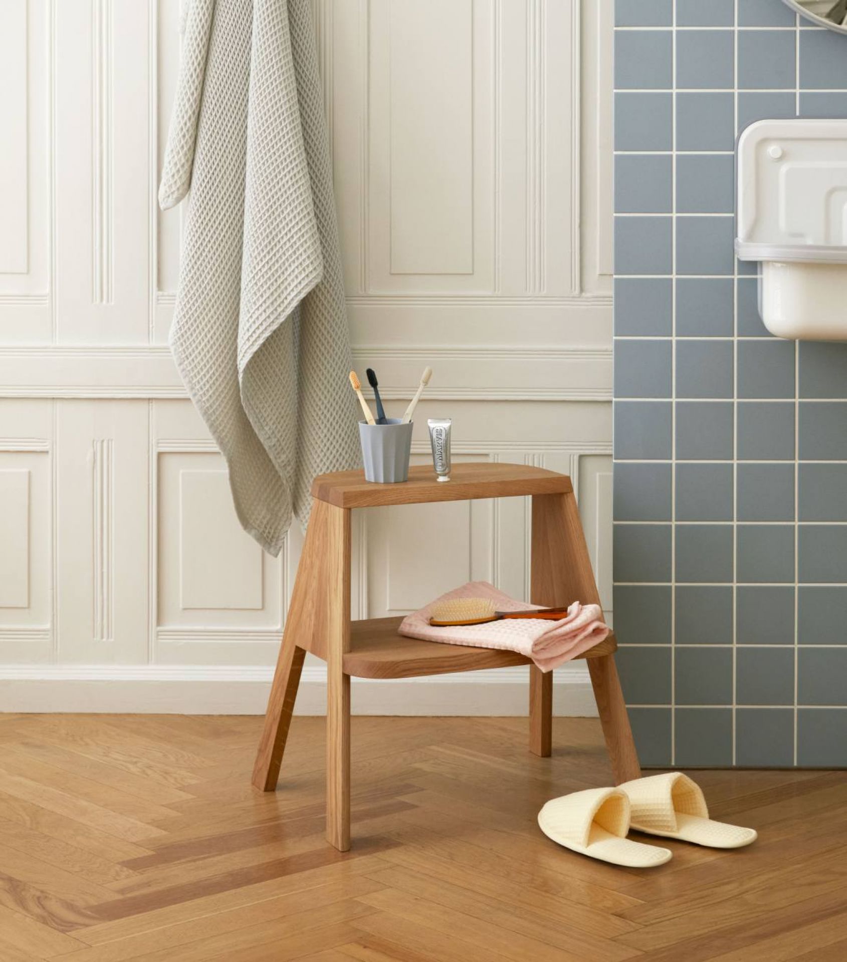 Hay Butler Hocker aus Holz im Badezimmer mit Handtuch, Zahnbürsten und Badeschuhen.
