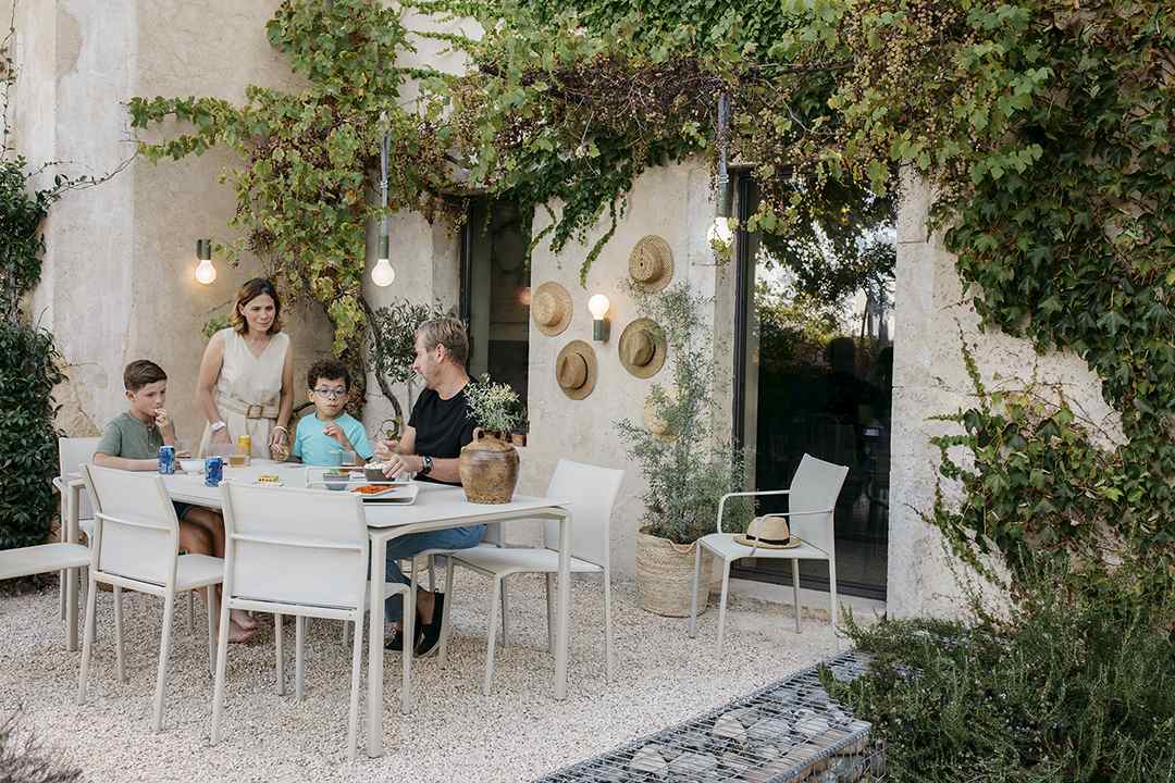 Familie sitzt am Calvi Tisch von Fermob im Garten und isst. Outdoor Möbel.
