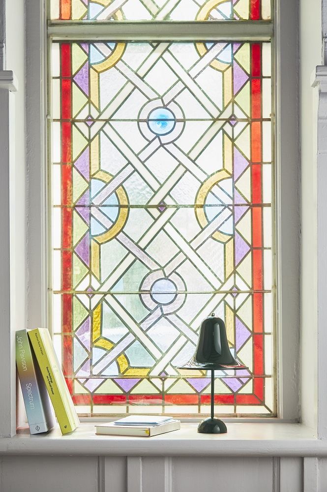 Pantop Portable Akkuleuchte von Verpan vor buntem Glasfenster, moderne Tischleuchte für Innen und Außen.