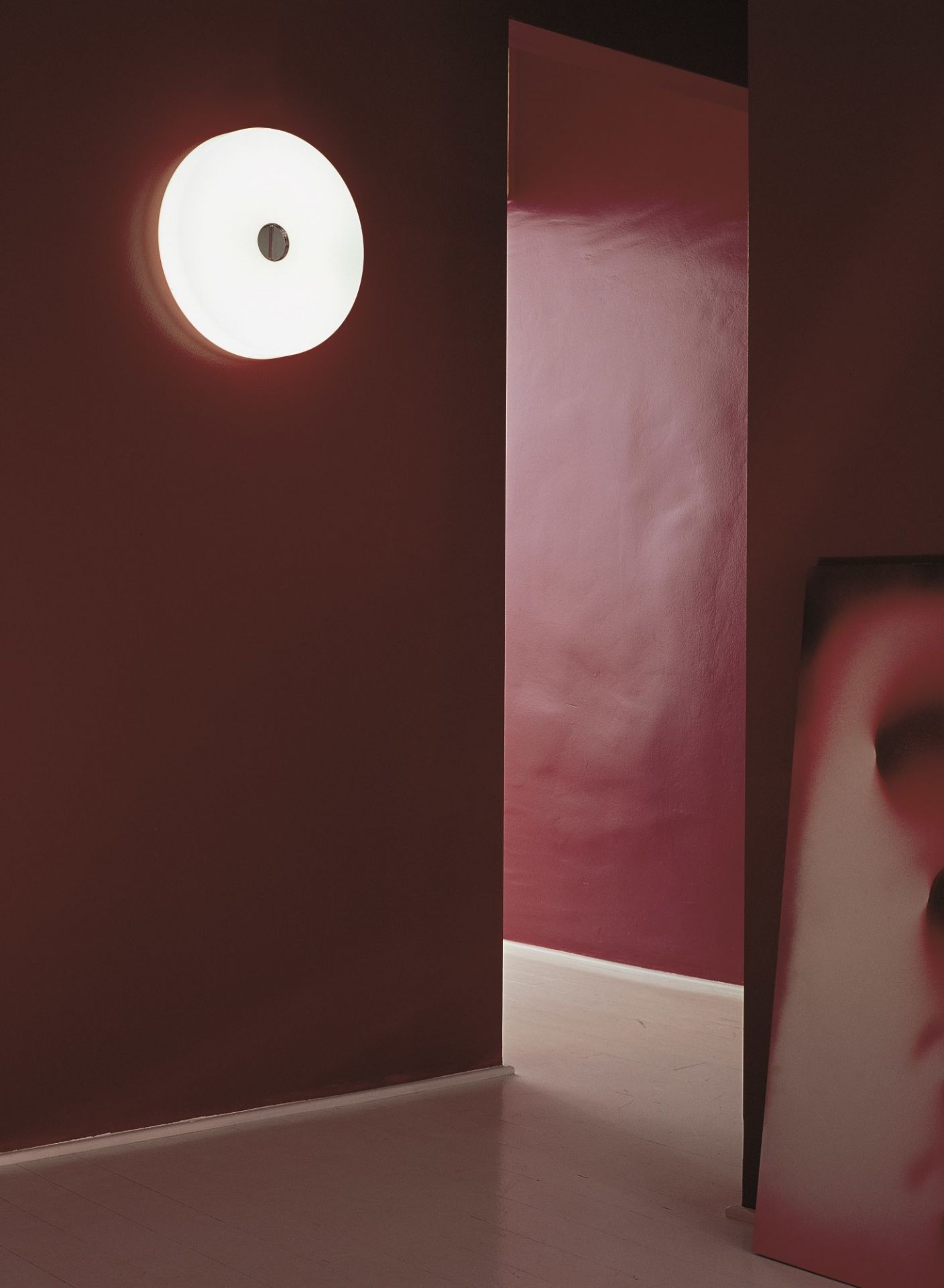 Runde Flos Wandleuchte, Modell Button HL, an einer dunkelroten Wand. Moderne Deckenleuchte.