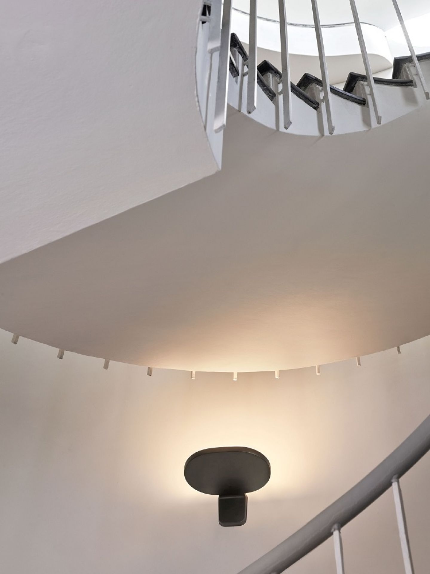 Weiße Oplight Wandleuchte von Flos an einer Wand unter einer Wendeltreppe. Modernes Design.