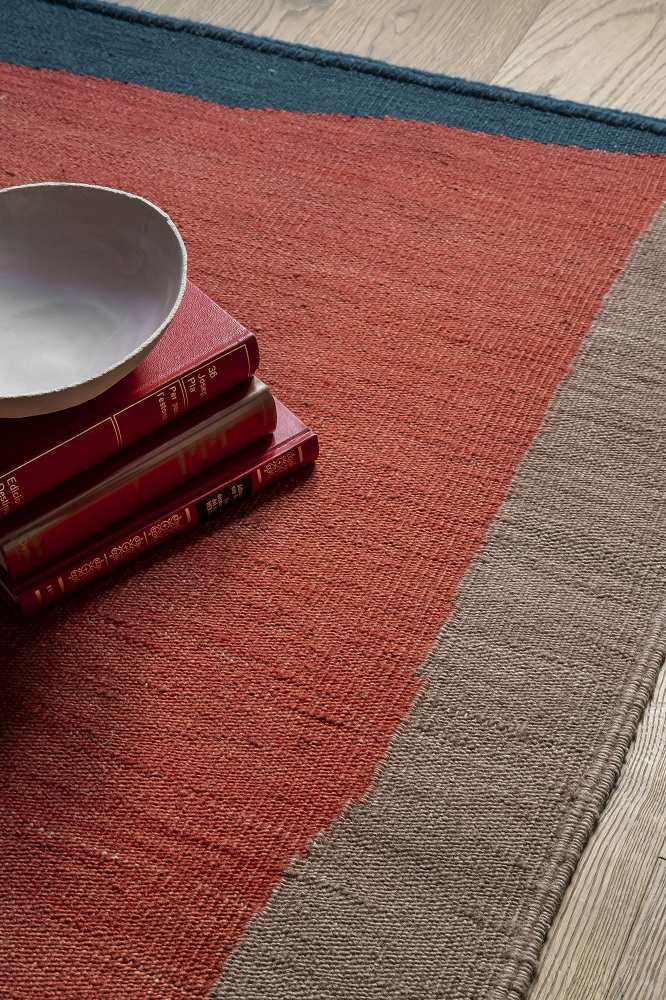 Detailaufnahme des Nanimarquina Tones Collection Kilim Teppichs in Rot, Braun und Blau mit Büchern und Schale.