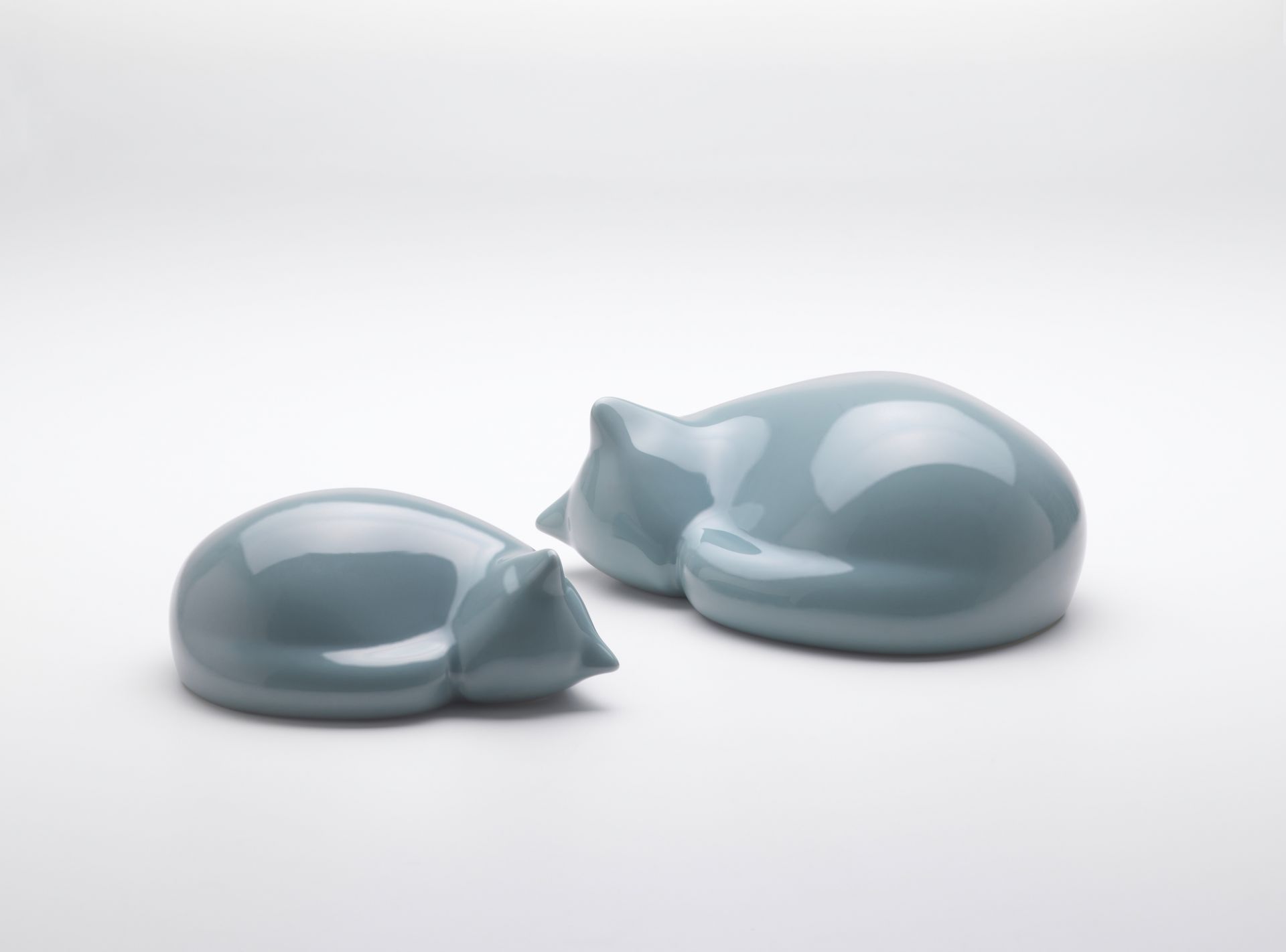 Zwei kleine, hellblaue Vitra Resting Cat Figuren liegen zusammengerollt auf weißem Hintergrund.