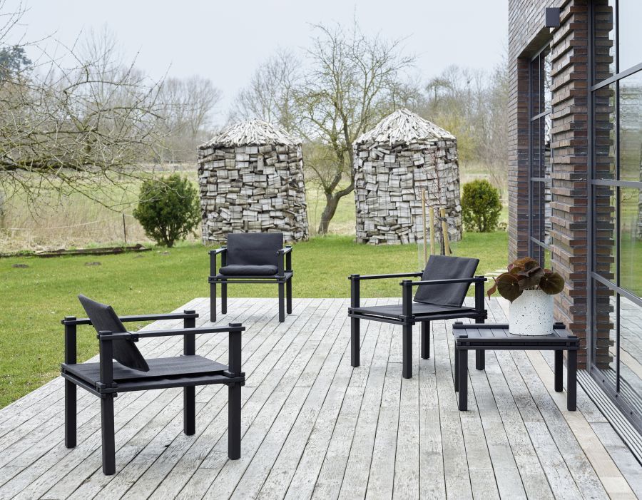 Drei schwarze Outdoor Sessel und ein Farmer Tisch auf einer Holzterrasse im Garten.