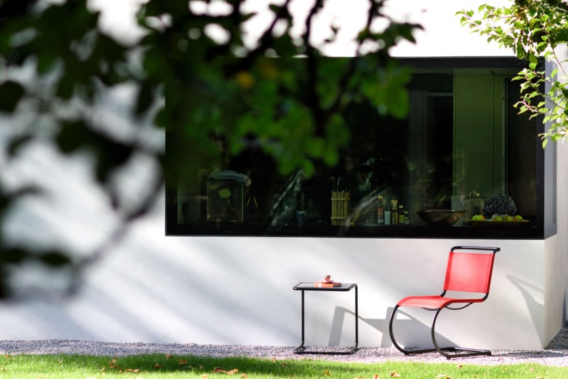 Thonet Beistelltisch Set B 9 im Außenbereich mit rotem Freischwinger Stuhl vor Fenster.