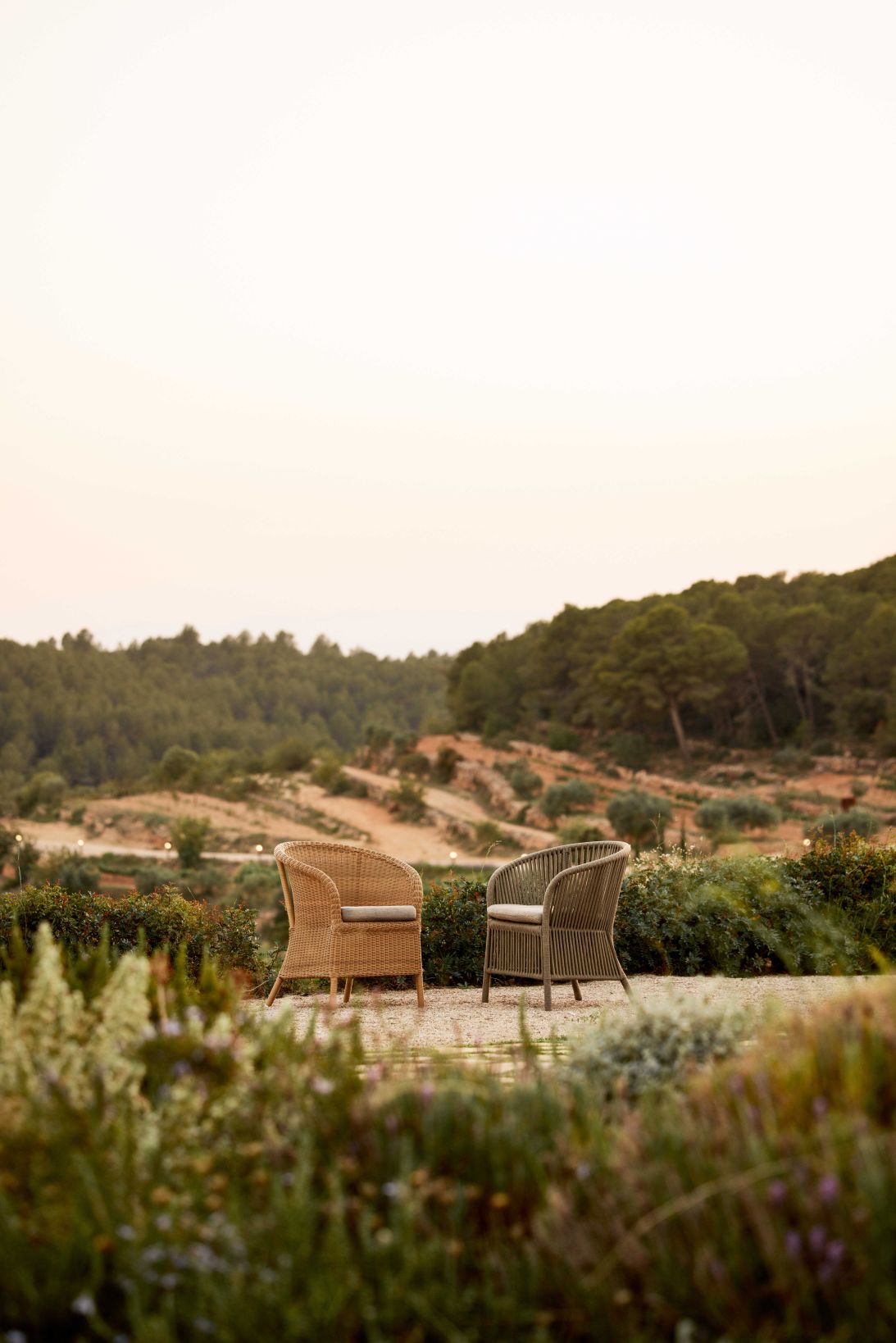Zwei Cane-Line Derby Outdoor Sessel aus Rattan auf einer Terrasse mit Landschaft im Hintergrund.