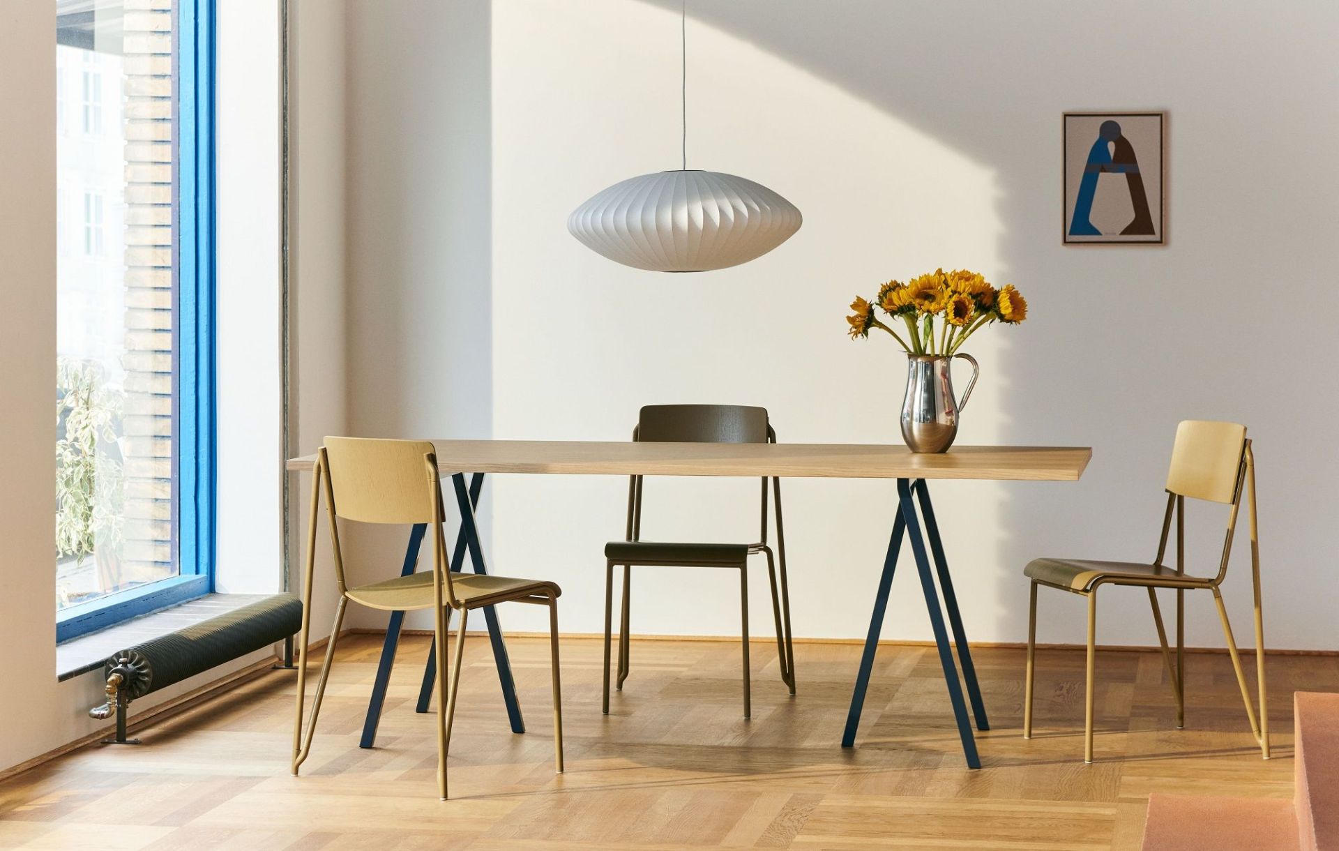 Heller Raum mit Hay Loop Stand Table Esstisch, Stühlen und Sonnenblumen in Vase.