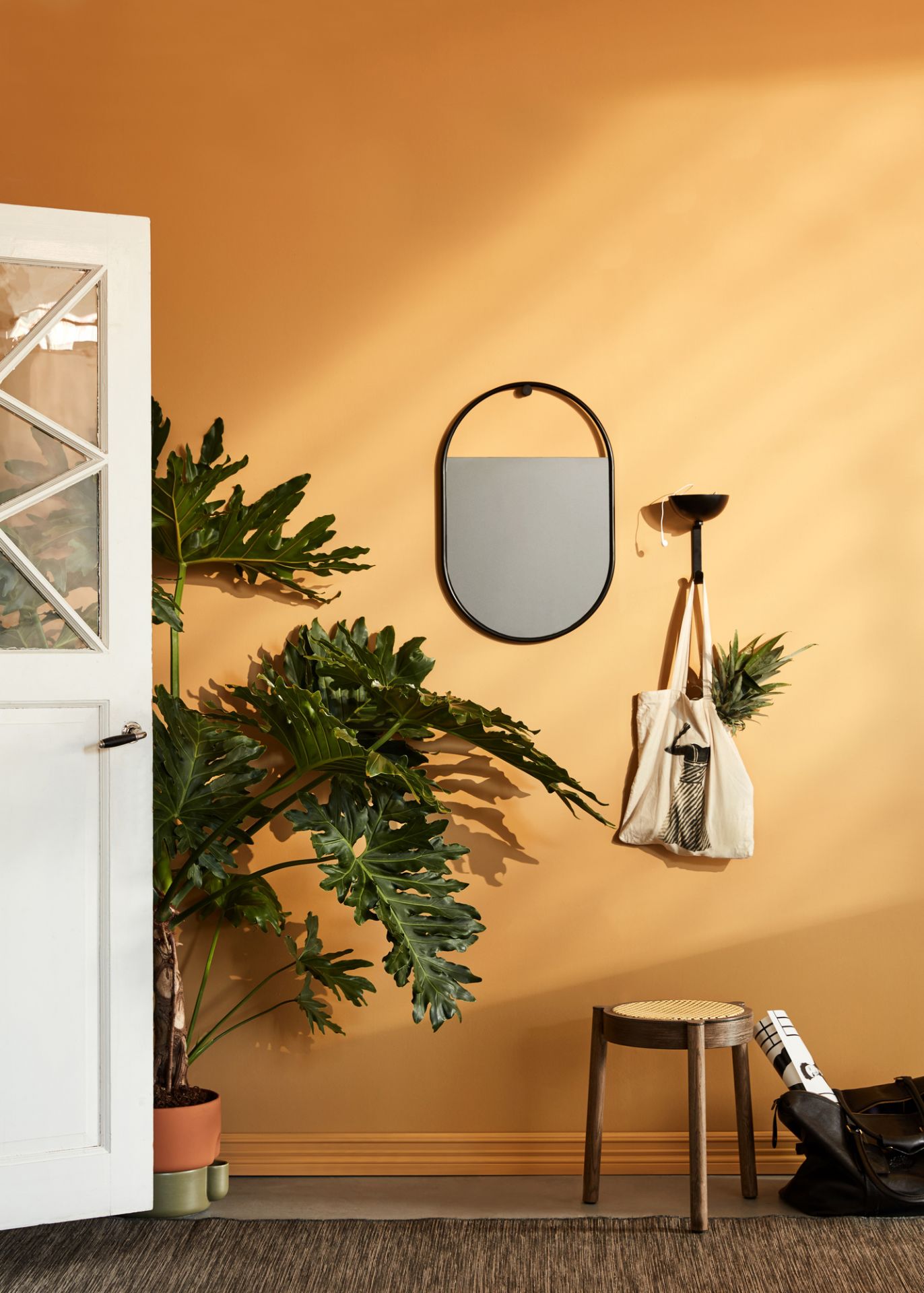 Ovaler Peek Wandspiegel von Northern mit schwarzem Rahmen an ockerfarbener Wand, kombiniert mit Dekoration.