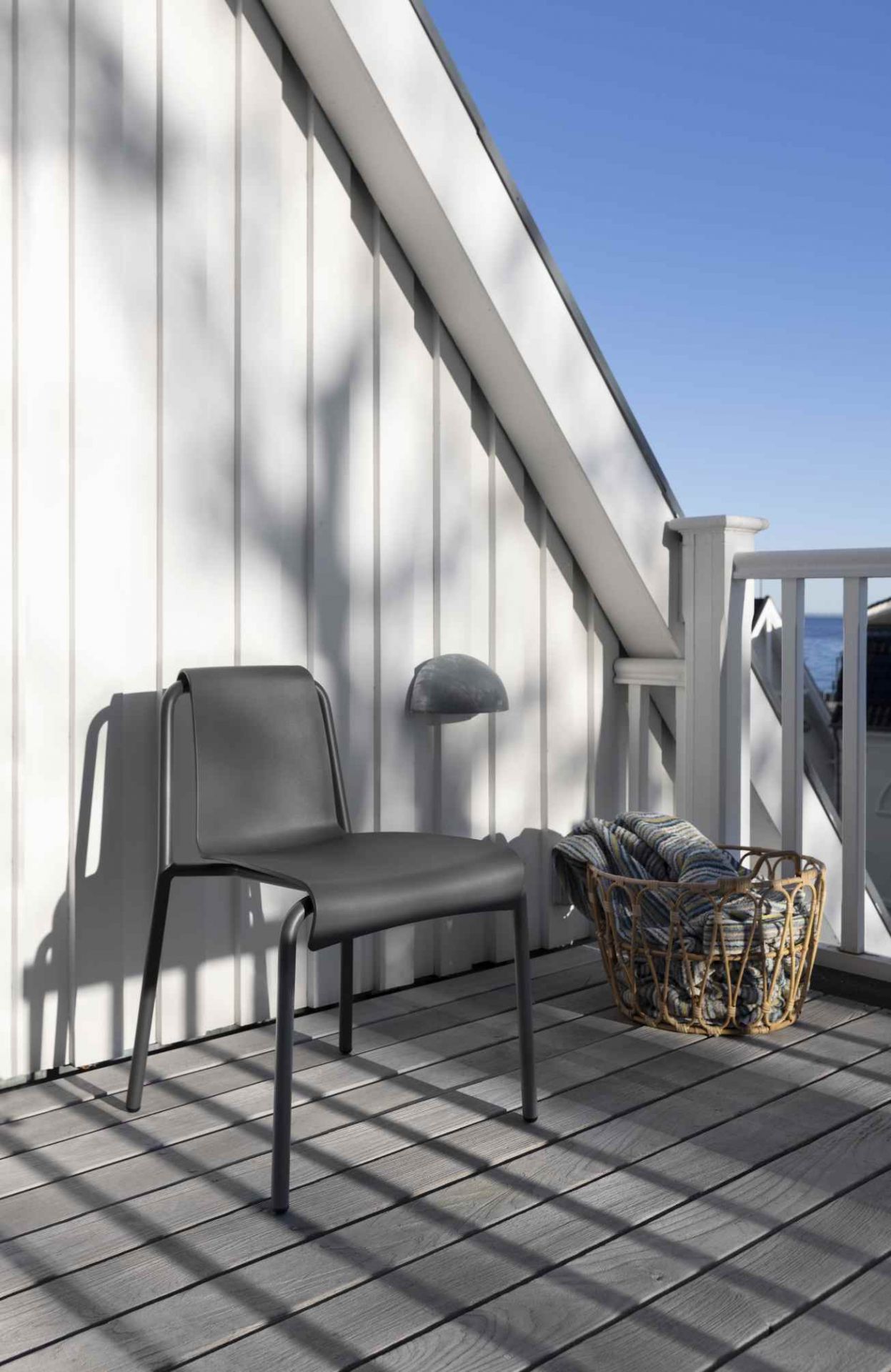 Grauer Nami Dining Chair Outdoor Stuhl von Houe auf einer Terrasse mit Korb und Decke.