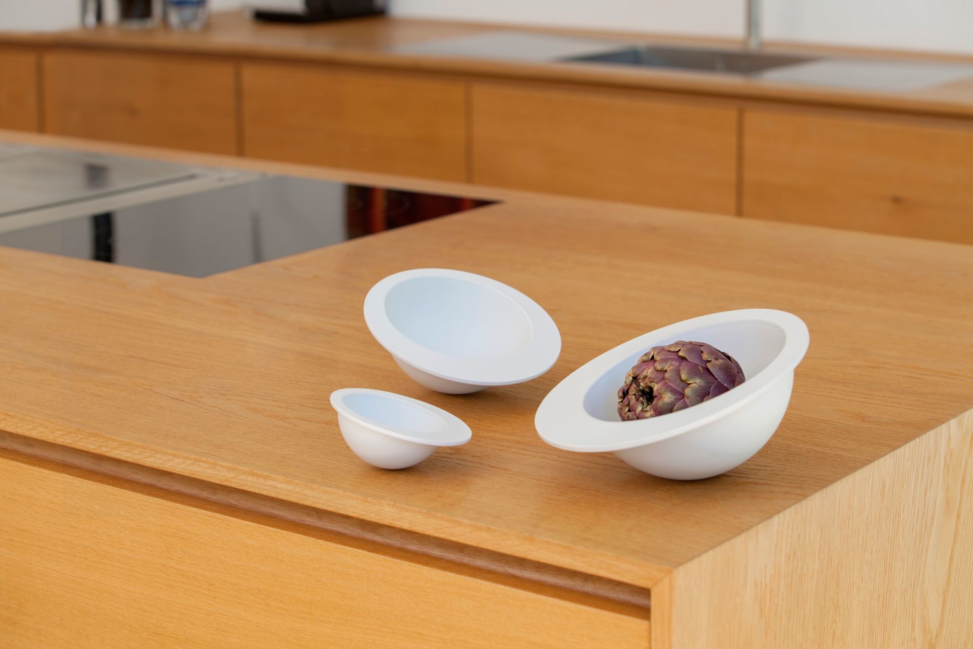 Drei weiße Schalen, darunter die Pivot Schale, auf einer hölzernen Küchentheke, eine mit Artischocke.