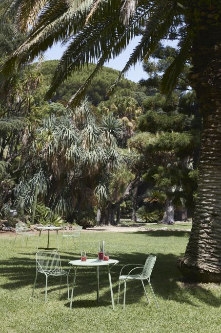 Grüner Hiray Outdoor Stuhl mit Armlehne von Kartell auf Rasen vor tropischer Kulisse. Gartenmöbel für Terrasse.