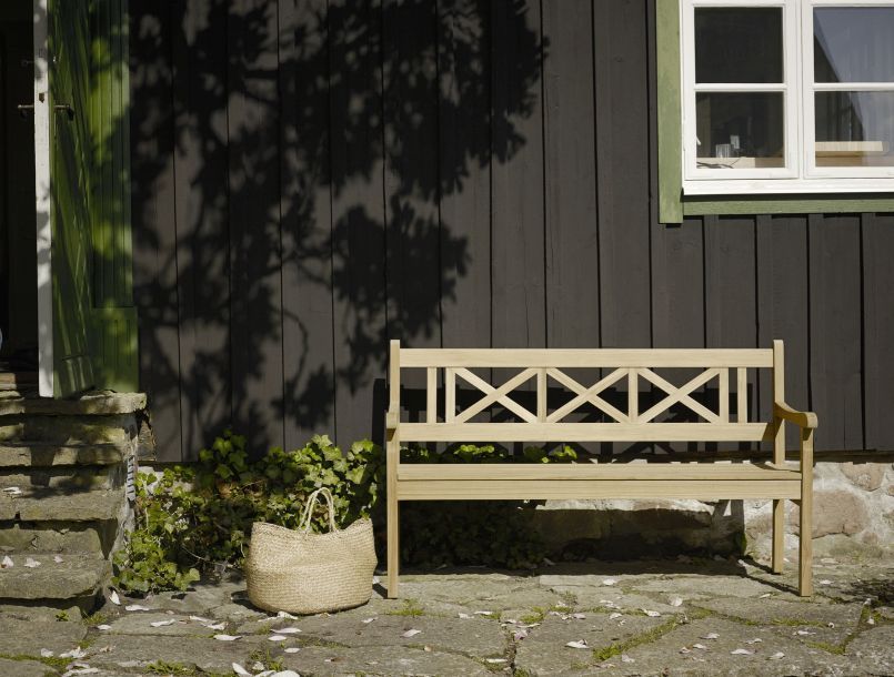 Skagen Gartenbank aus Holz vor dunkler Holzwand, ideal für Garten und Terrasse.