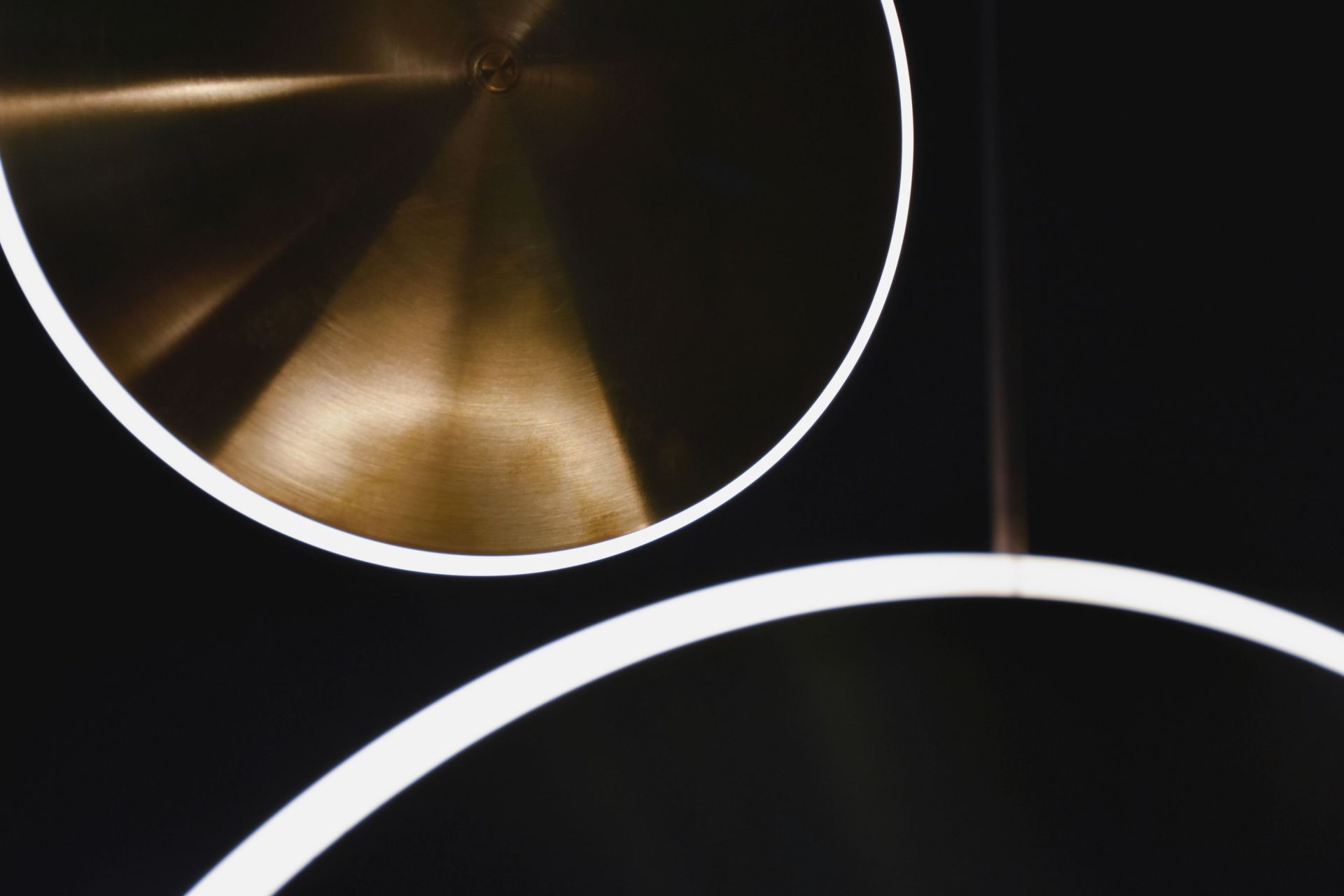 Detailaufnahme der Sconce10 Chrona Wandleuchte von Graypants: Messingfarbene Scheibe mit LED-Lichtring vor dunklem Hintergrund.