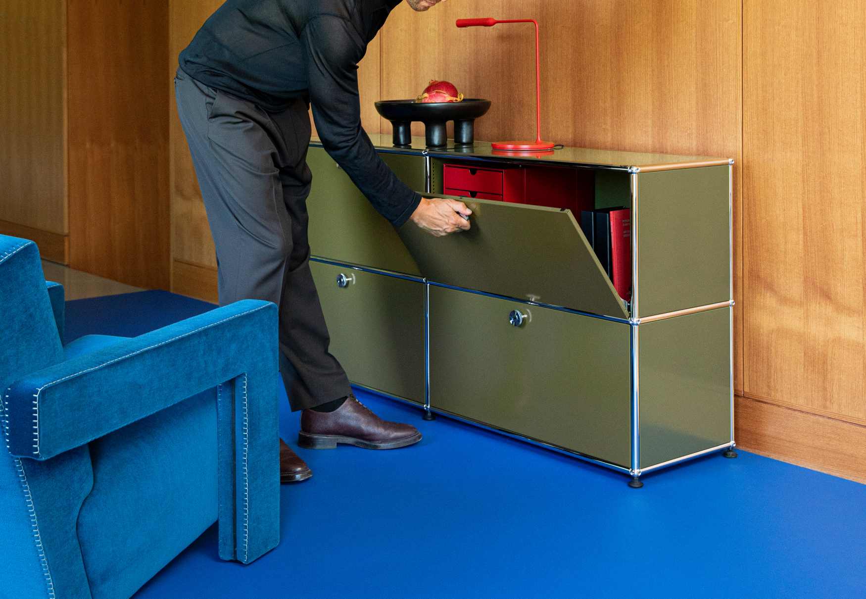 USM Haller Sideboard in Olivgrün mit vier Klapptüren, eine Tür wird geöffnet, modernes Wohnzimmermöbel.