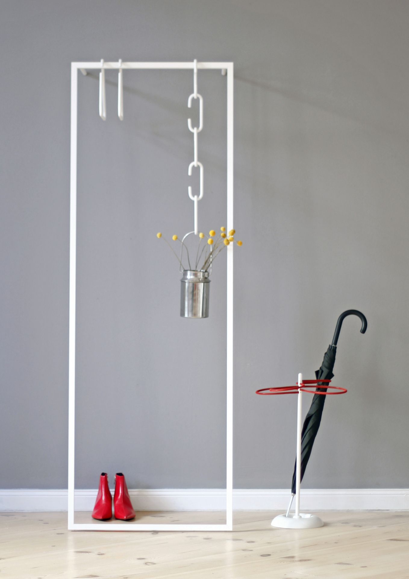 Weiße Leano Anlehngarderobe von Roomsafari mit Regenschirm, roten Schuhen und Dekoration vor grauer Wand.