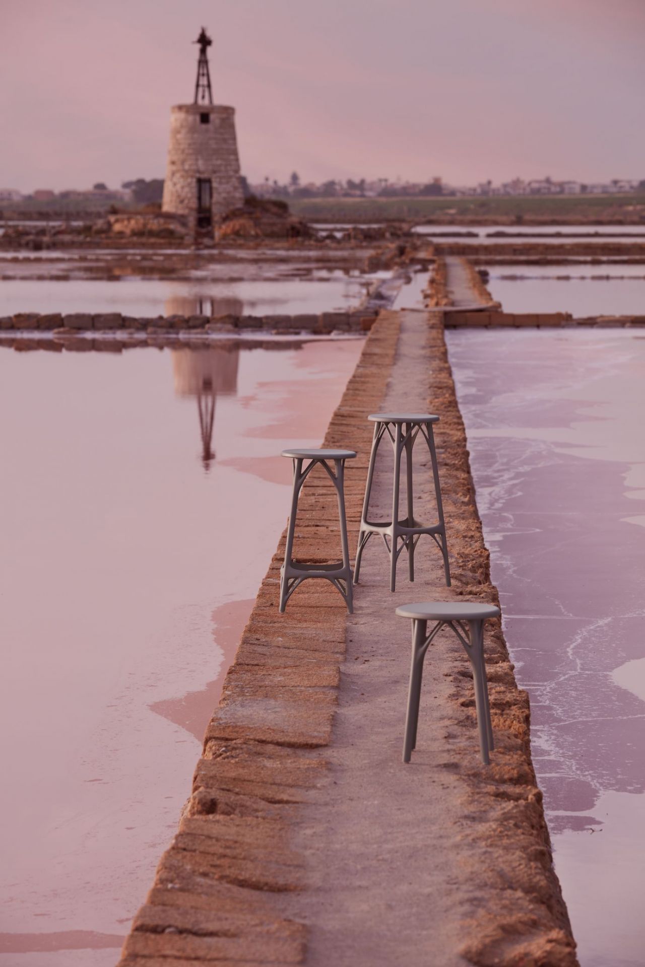 Drei graue A.I. Hocker von Kartell auf einem Steg vor einer Saline. Design Hocker.