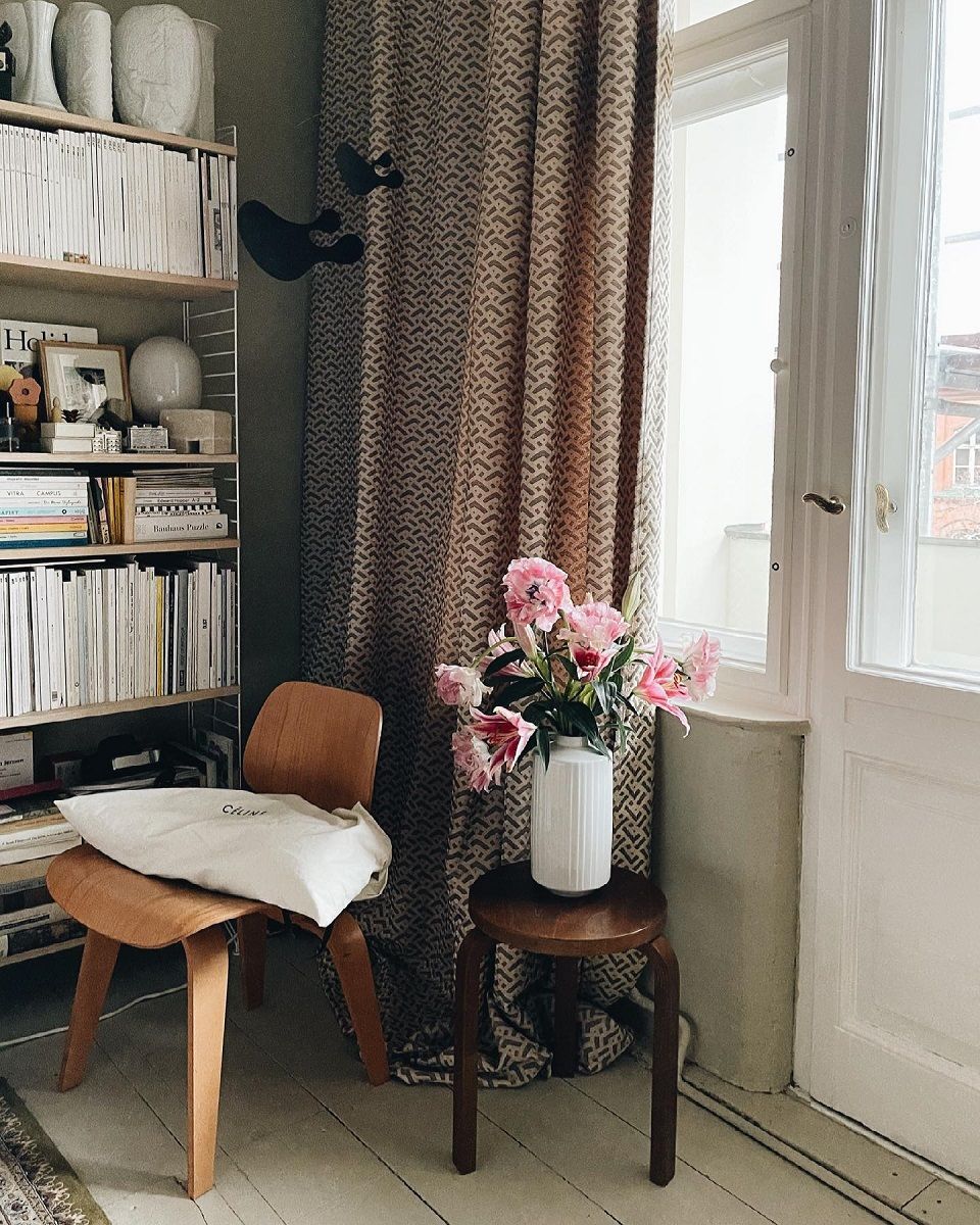 Vitra Plywood Group DCW Holzstuhl in natürlicher Umgebung mit Bücherregal und Blumen.