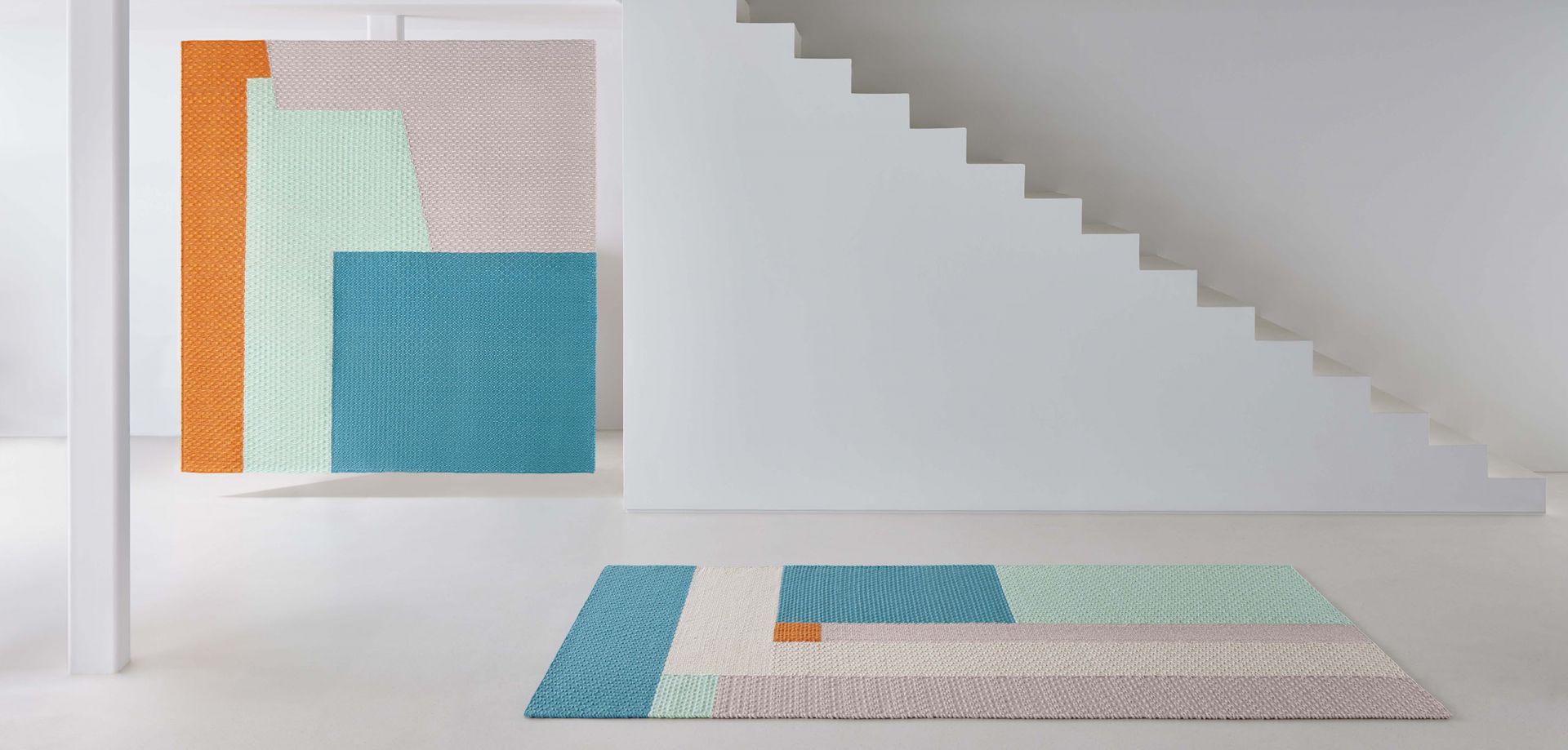 Weave Rug Teppich Space Hopper Gan mit geometrischem Muster in Pastellfarben und Orange in minimalistischem Raum.