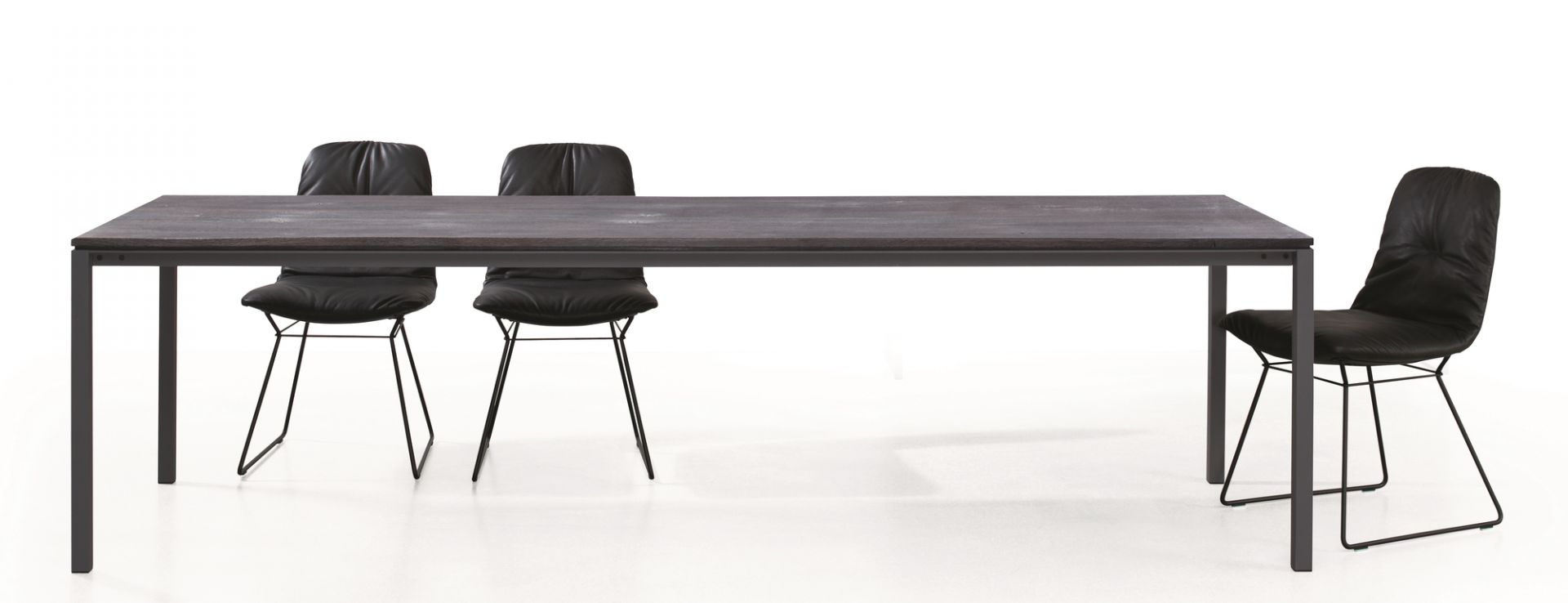 S 600 Tisch von Janua mit geölter Eichenplatte und schwarzen Stühlen vor weißem Hintergrund.