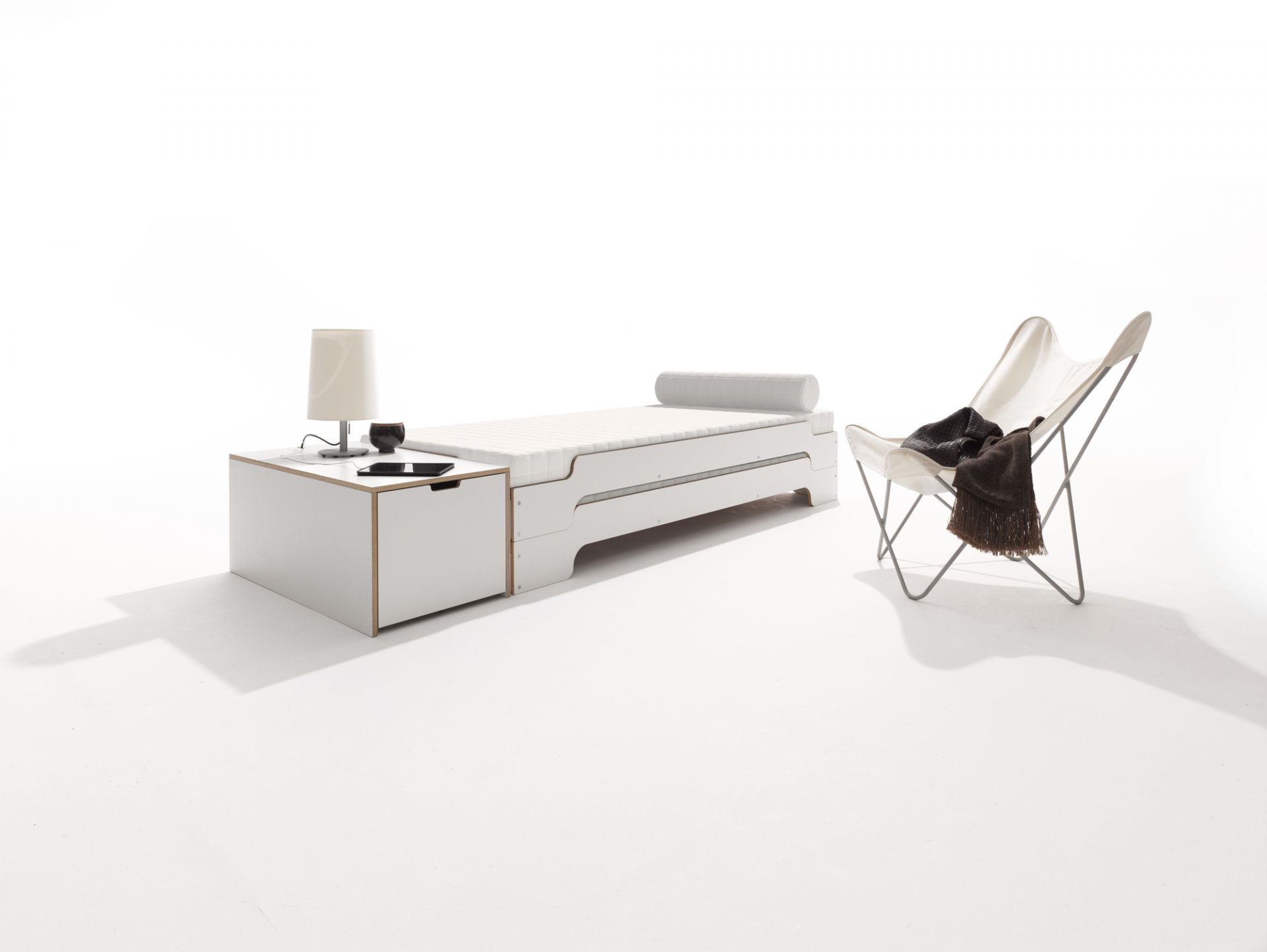 Klassik Bettkasten 16 von Müller Möbelwerkstätten mit Schubkasten, Nachttisch und Sessel auf weißem Hintergrund.