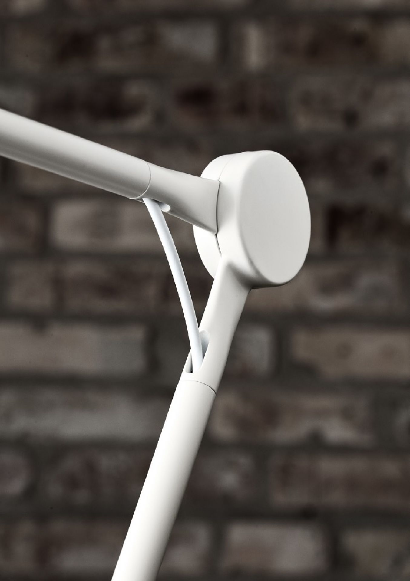Detailaufnahme der weißen Fritz Hansen AQ01 Tischleuchte: Gelenk und Kabel vor Backsteinwand.