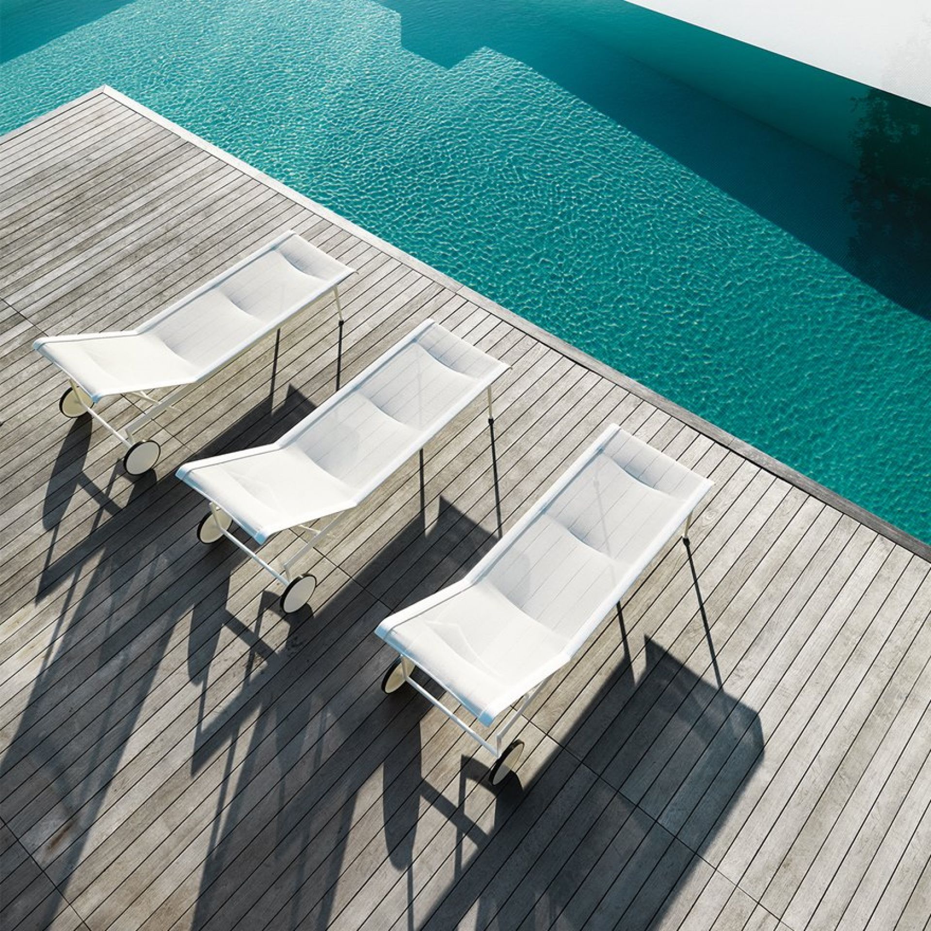 Drei weiße Richard Schultz Liegen auf Holzdeck neben einem Pool. Outdoor Möbel.