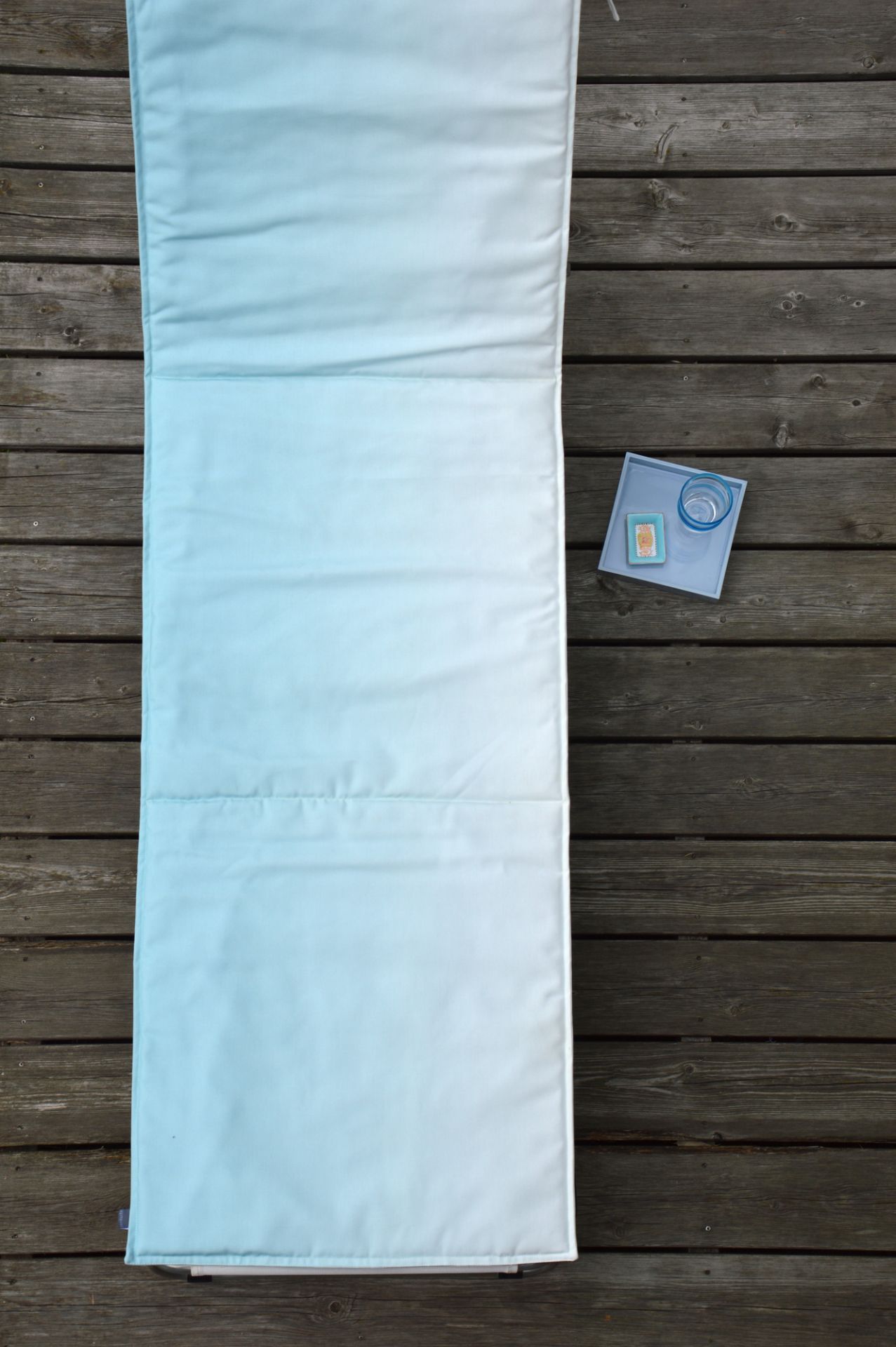 Luxury Auflage Padua Aqua von Jan Kurtz auf Holzterrasse mit Getränken.