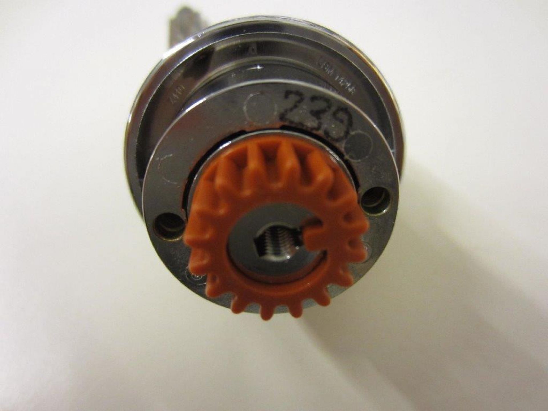 Nahaufnahme des USM Haller Schloss Ersatzteils mit orangefarbenem Zahnrad und silberner Mechanik.