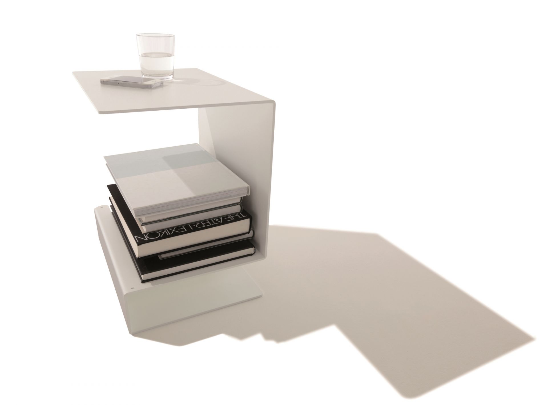 Weißer Huk Beistelltisch von Müller Möbelwerkstätten mit Büchern, Glas Wasser und Smartphone.