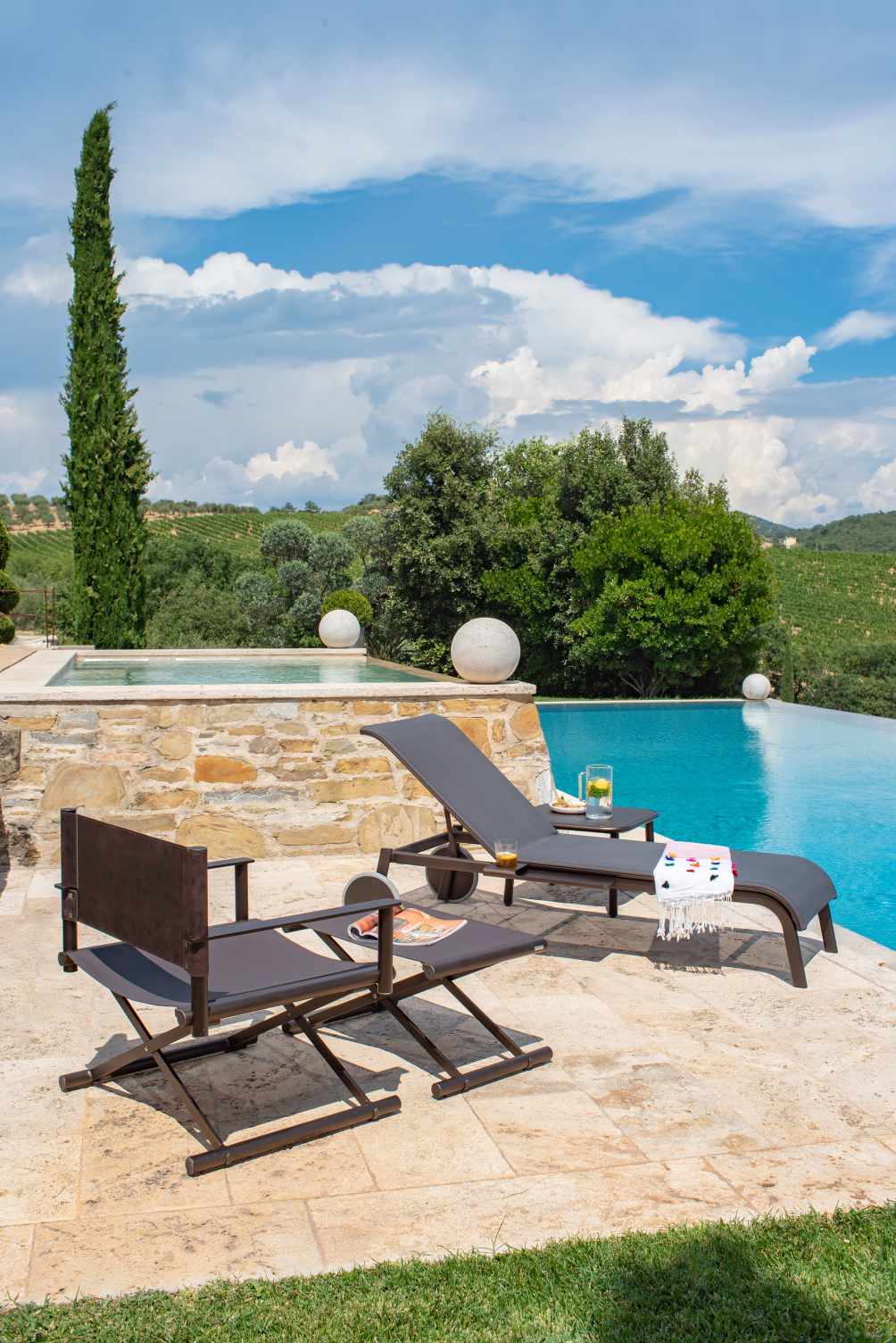 Terra Lounge Chair Sessel von Emu und eine Sonnenliege am Pool mit mediterraner Landschaft.