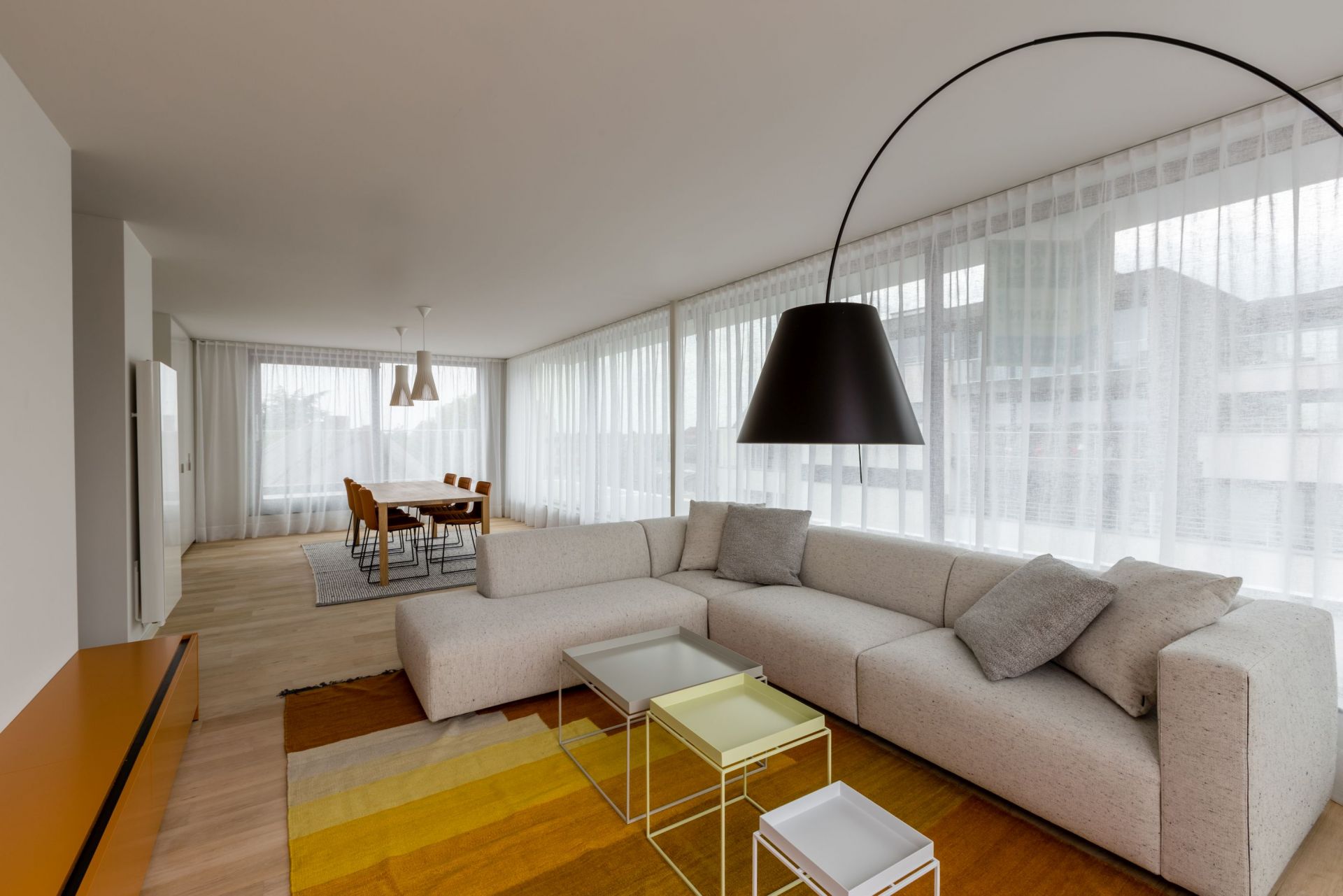 Helles Wohnzimmer mit großem, beigen Match Sofa von Prostoria und farbenfrohem Teppich.