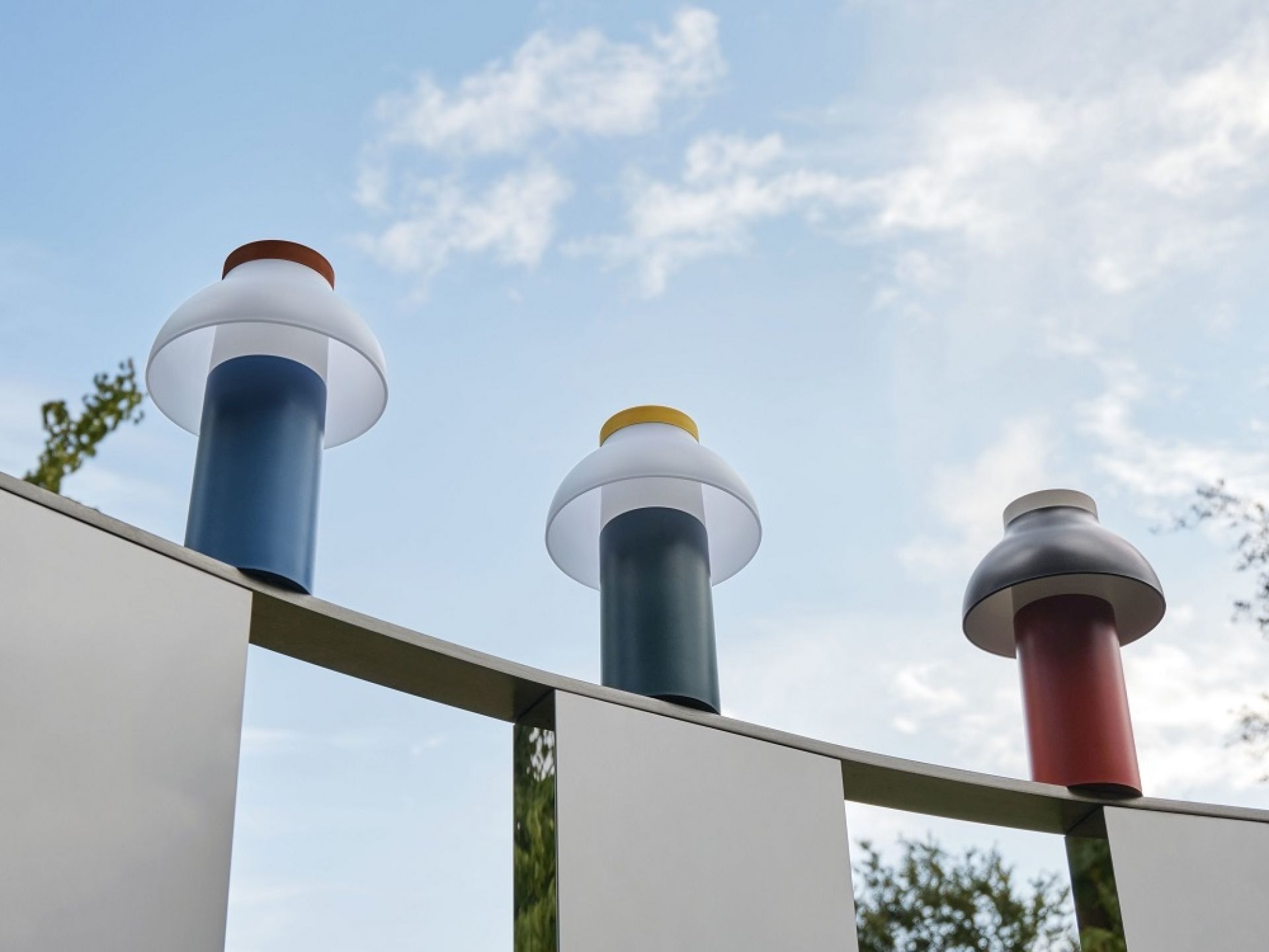 Drei PC Portable Akkuleuchten von Hay in verschiedenen Farben auf einer Mauer.