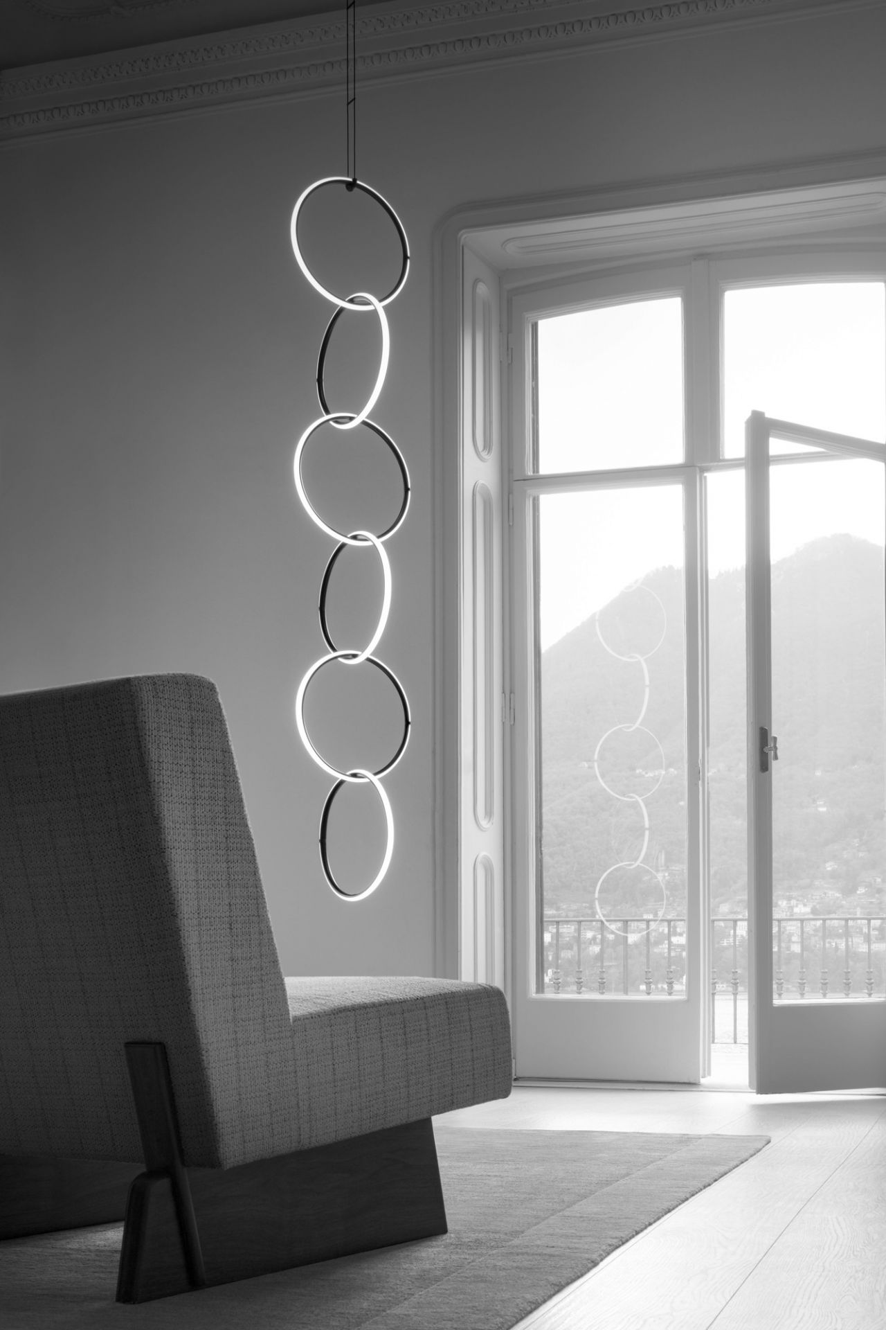 Arrangements Pendelleuchte von Flos: Moderne Hängeleuchte mit leuchtenden Ringen in einem minimalistischen Wohnraum.