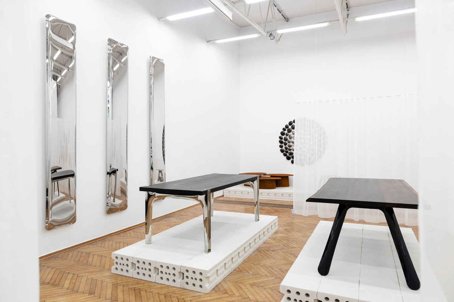 Ausstellungsraum mit Nogi Tischgestell von Zieta, schwarze Tischplatte, glänzende Metallbeine auf weißem Podest.